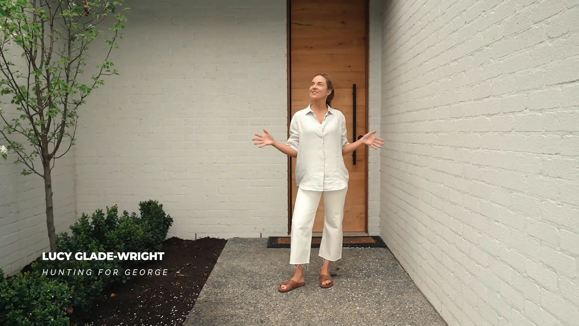 Lucy Glade-Wright at the entry of Ivy Lane Residence, framed by white brick walls and a timber door, introducing the home’s inward-looking, courtyard-focused layout.