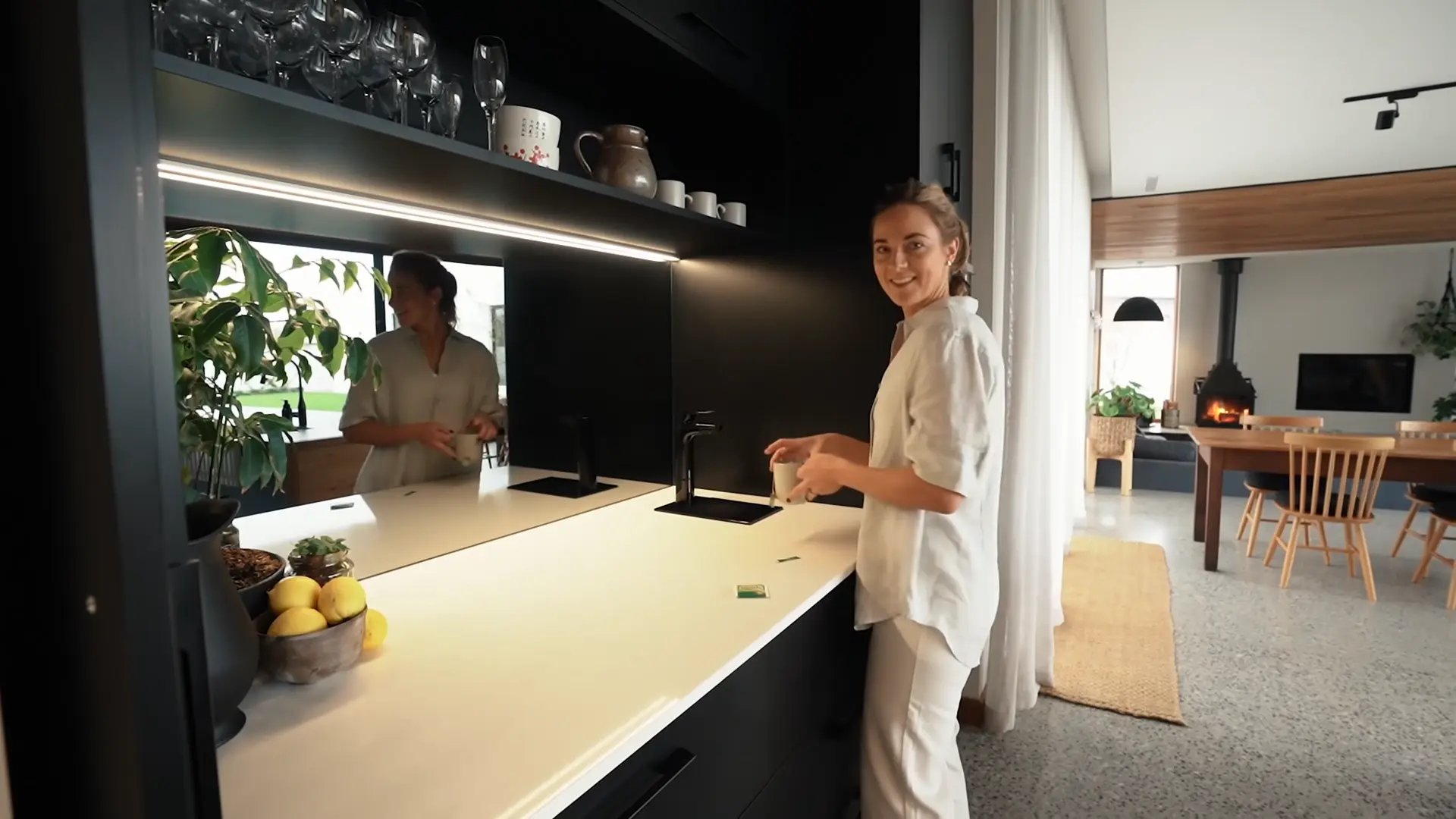 Lucy Glade-Wright uses the kitchen, a dark-toned space with integrated lighting, concealed storage, and a minimalist side kitchen bench opening to the living area beyond.