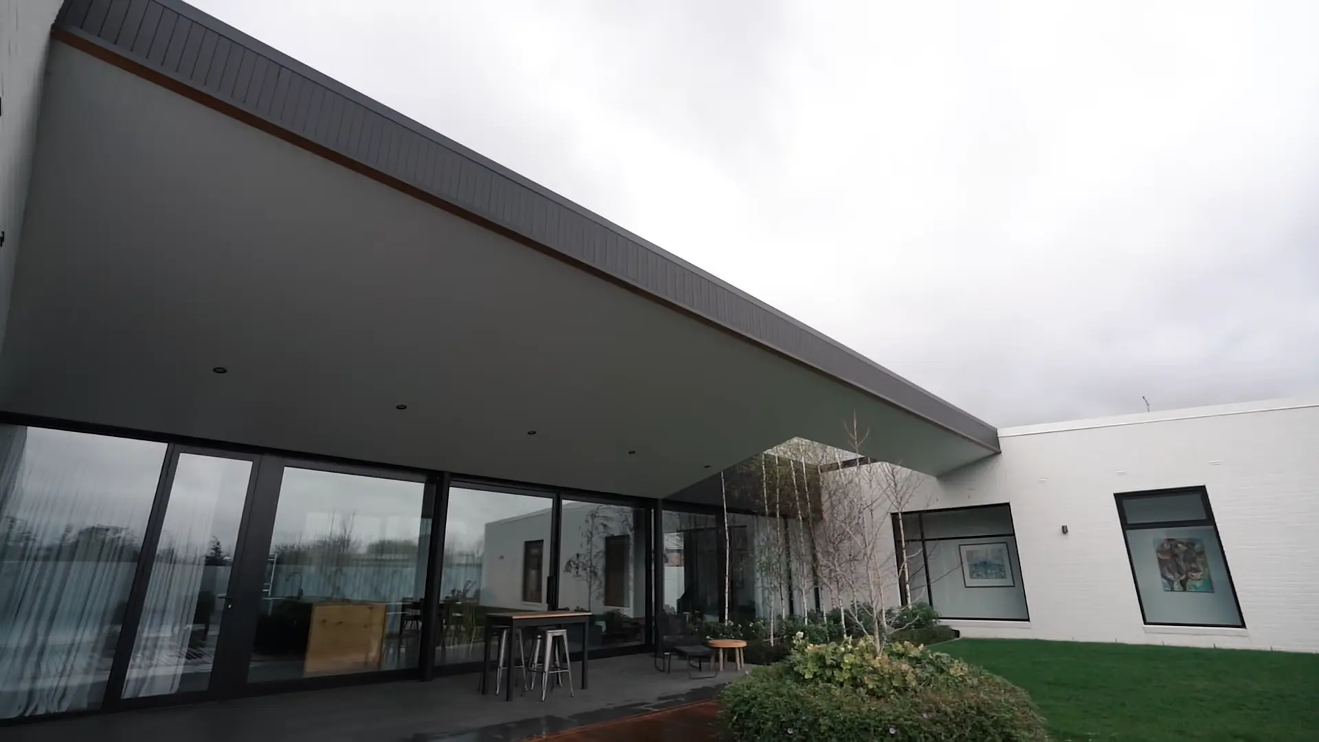 A still of the private courtyard with surrounding glazing, deep eaves, and landscaped garden, creating a sheltered indoor–outdoor living environment.