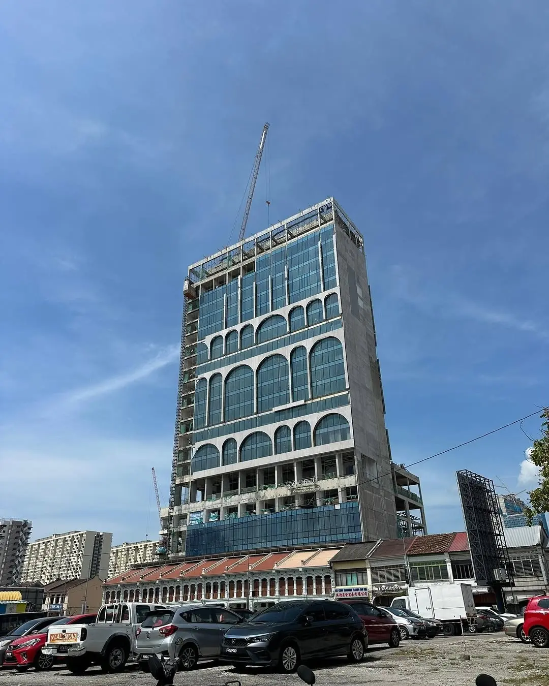 A tall skyscraper under construction featuring a distinctive glass facade with large arched window designs, towering over a row of traditional low-rise historic buildings