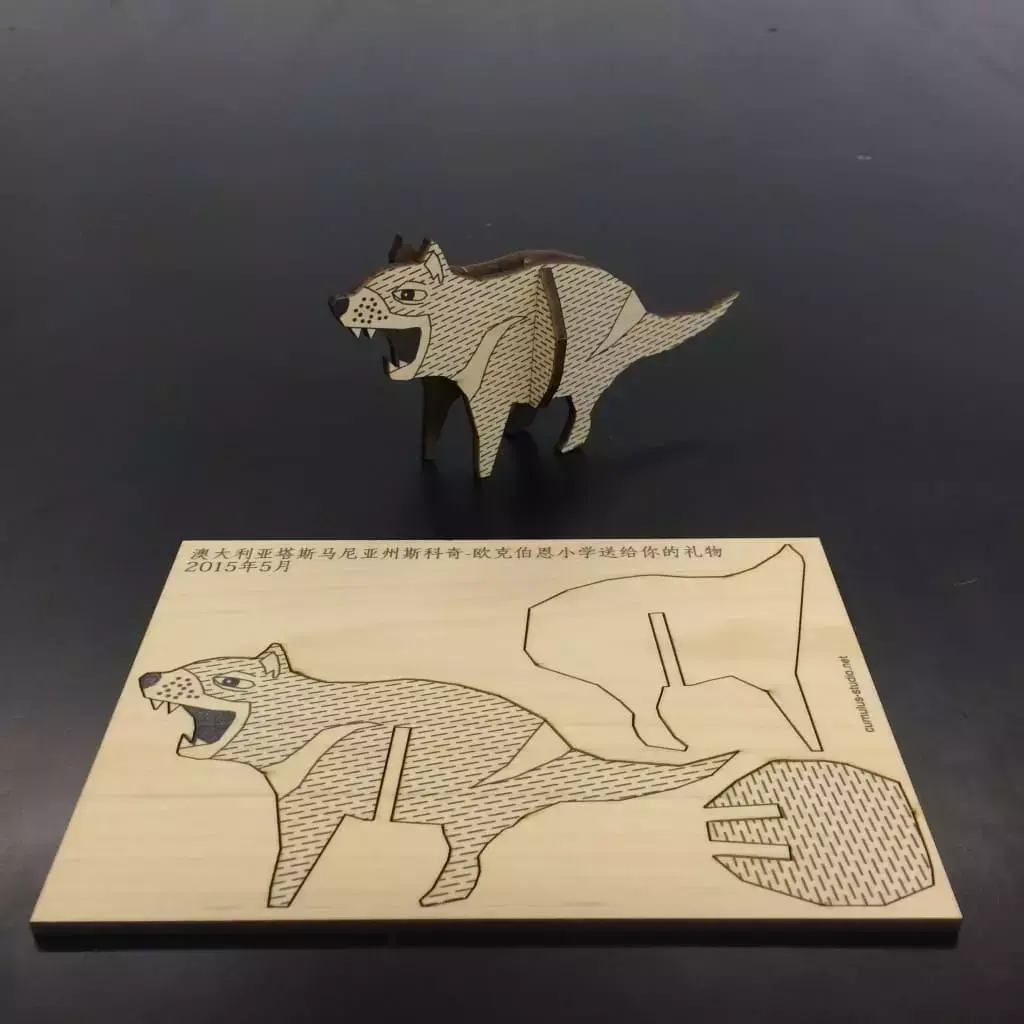 A small, ornate 3D wooden Tassie Devil completed and standing, with a 2D construction kit to make the sculpture sitting in front, made of golden sassafras and blackwood timber veneer,