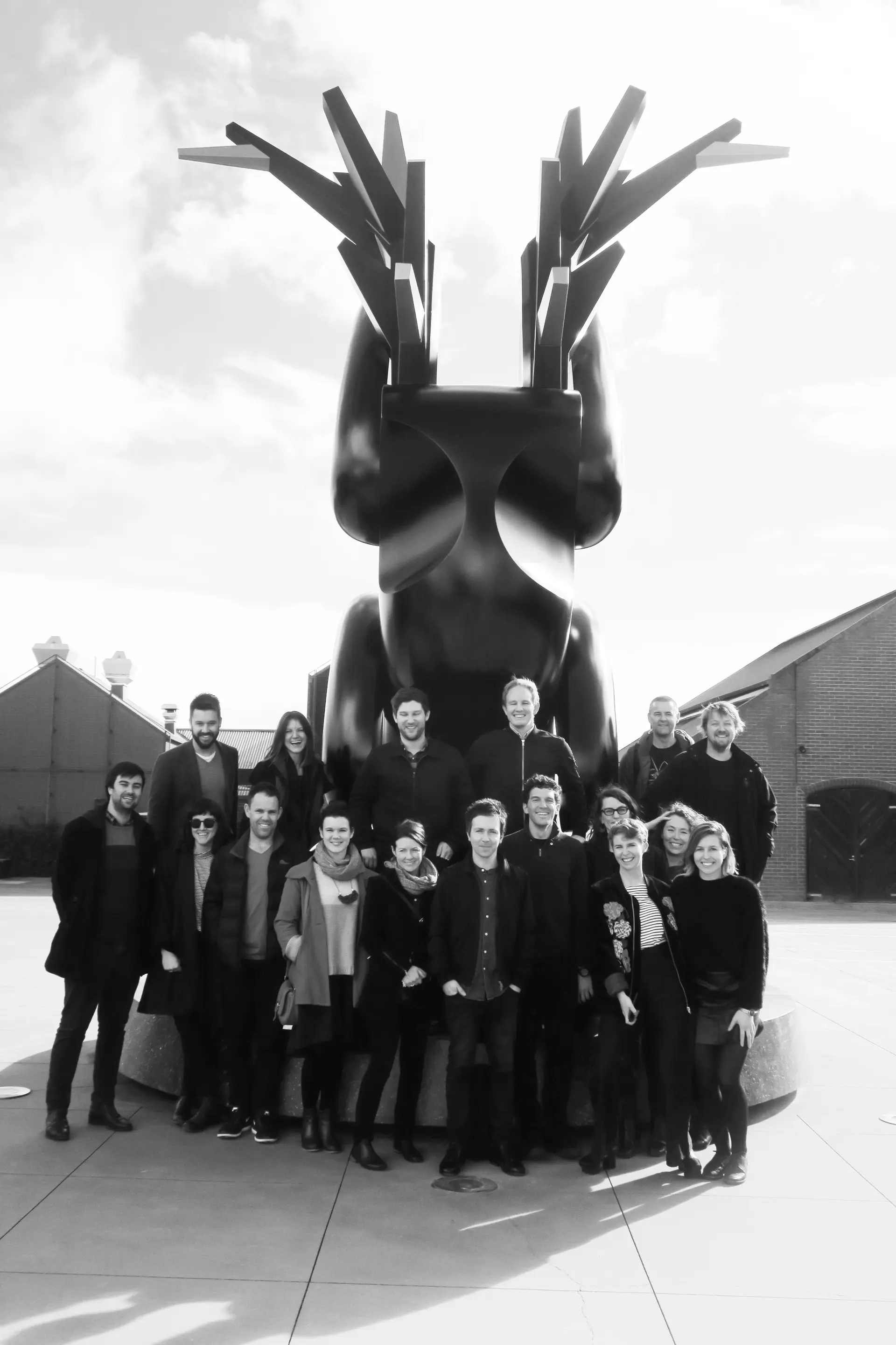 A black and white photo of the team at Cumulus smiling in front of a statue.