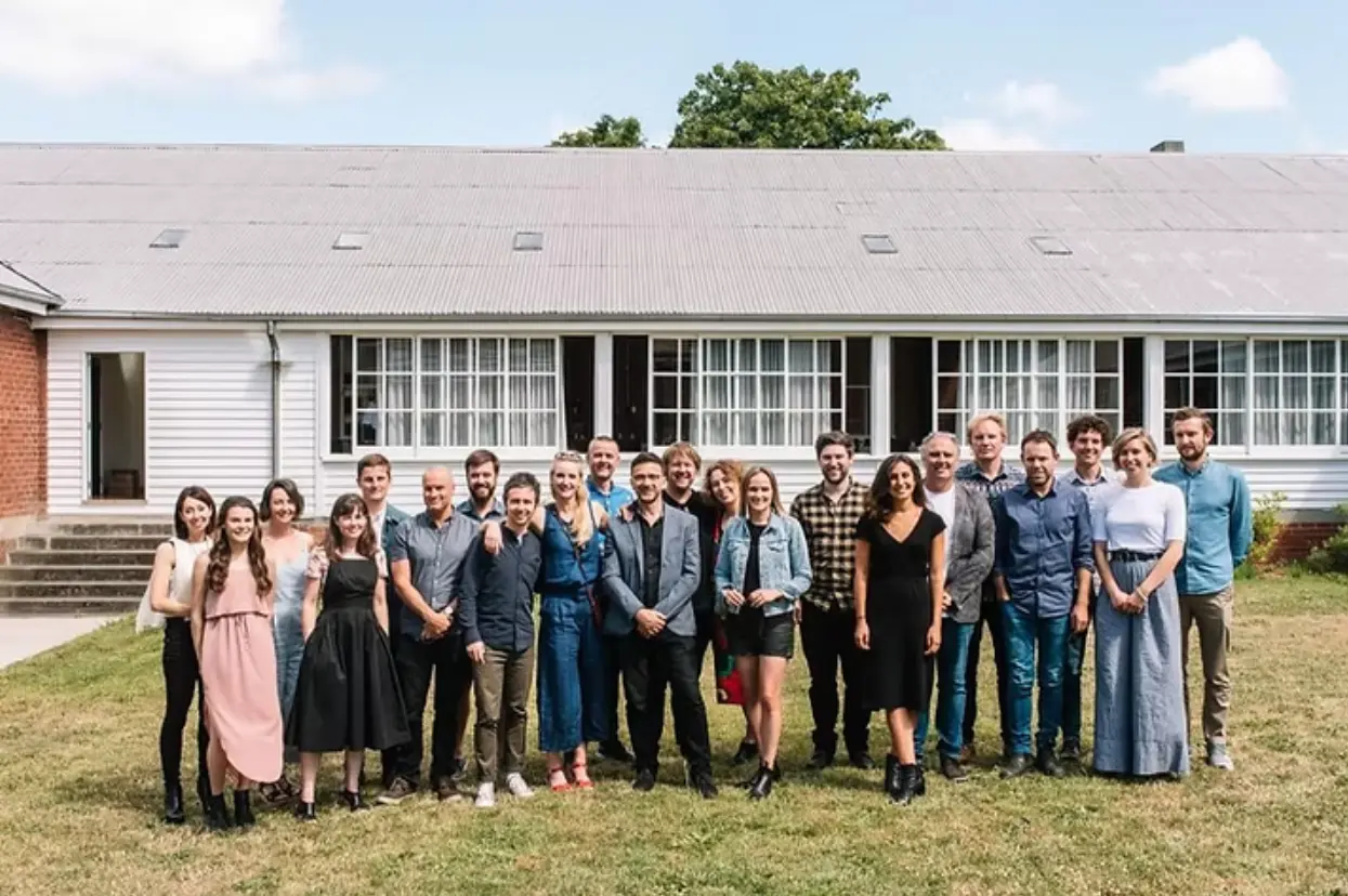 Our team gathered outdoors in front of a long, white heritage building, posing together on a grassy lawn for a group photo at the end of the year.
