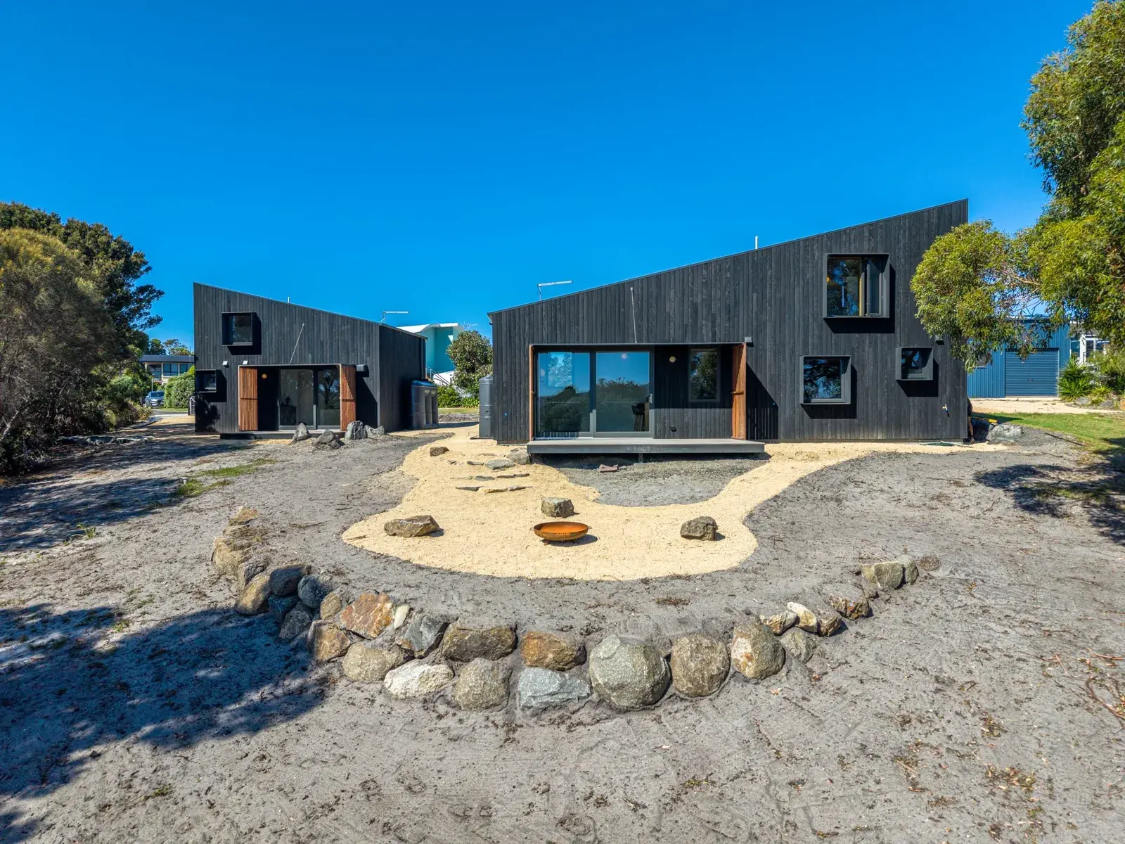 Two black houses with a driveway and rocks