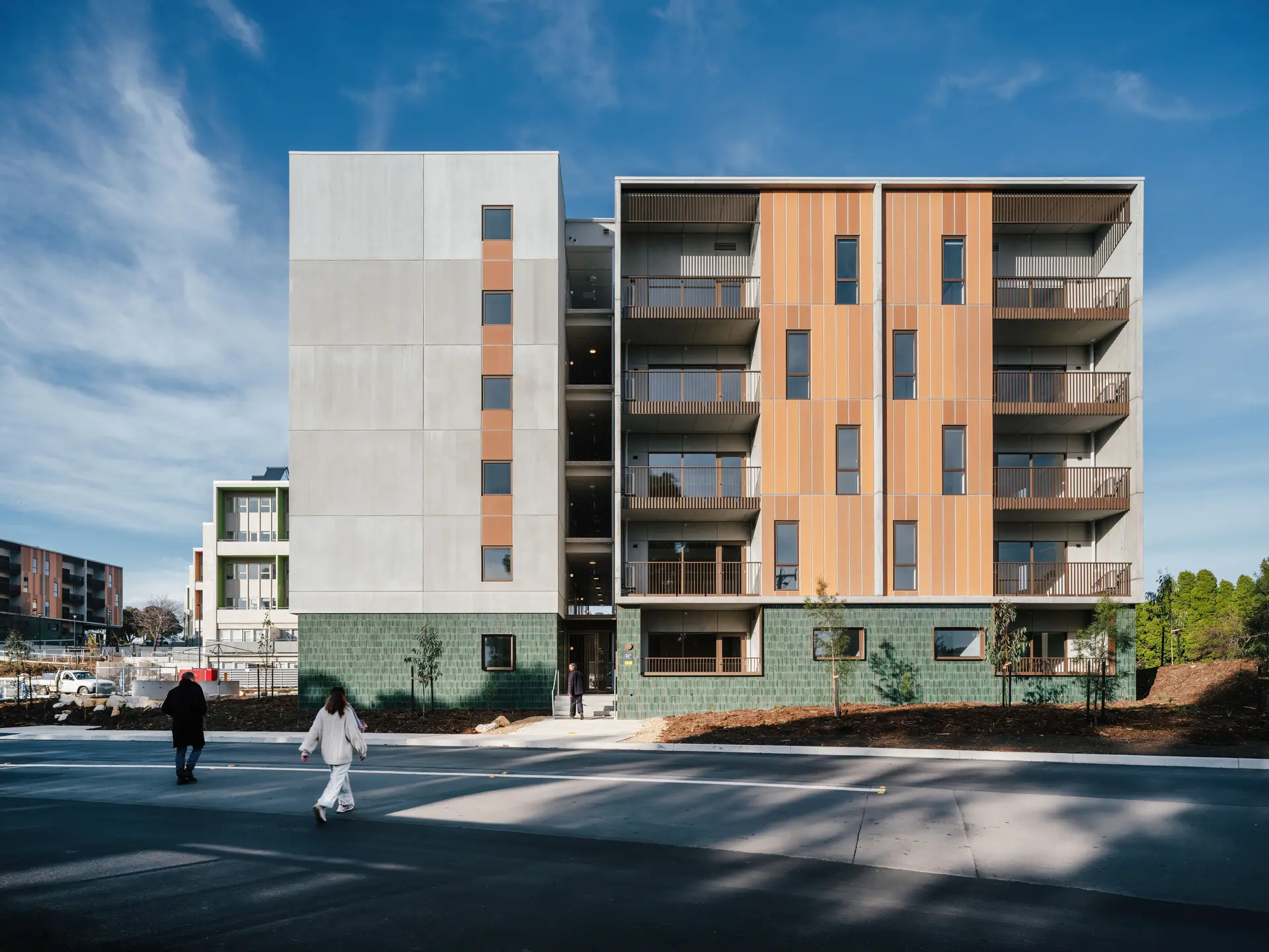 A unit complex in the shade, with two people walking across the street.