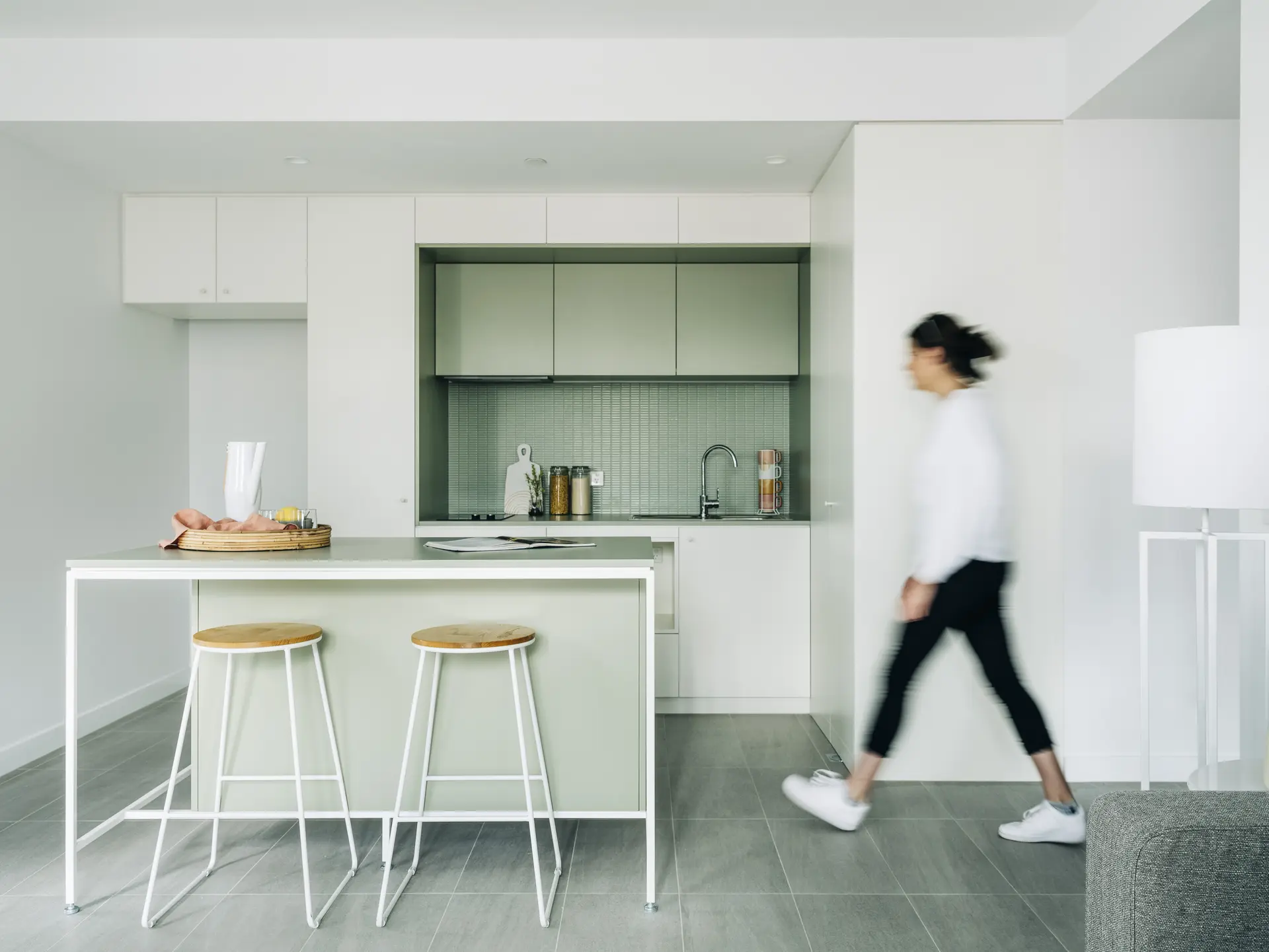 A person walking through a white kitchen with green cabinetry.