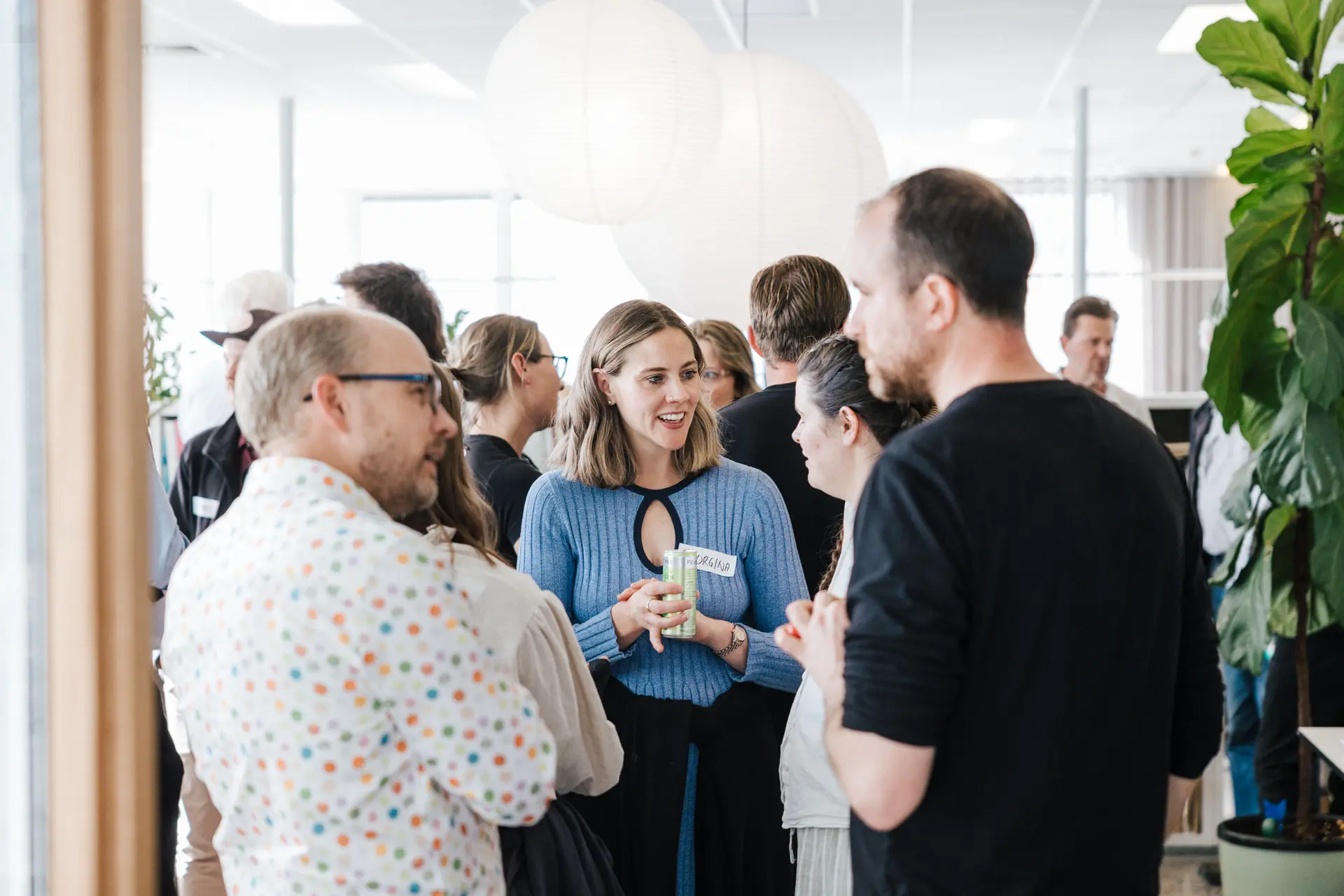 A group of people chatting at the Hobart end of year celebrations in the Hobart office, featuring large white paper lantern lights and indoor plants.