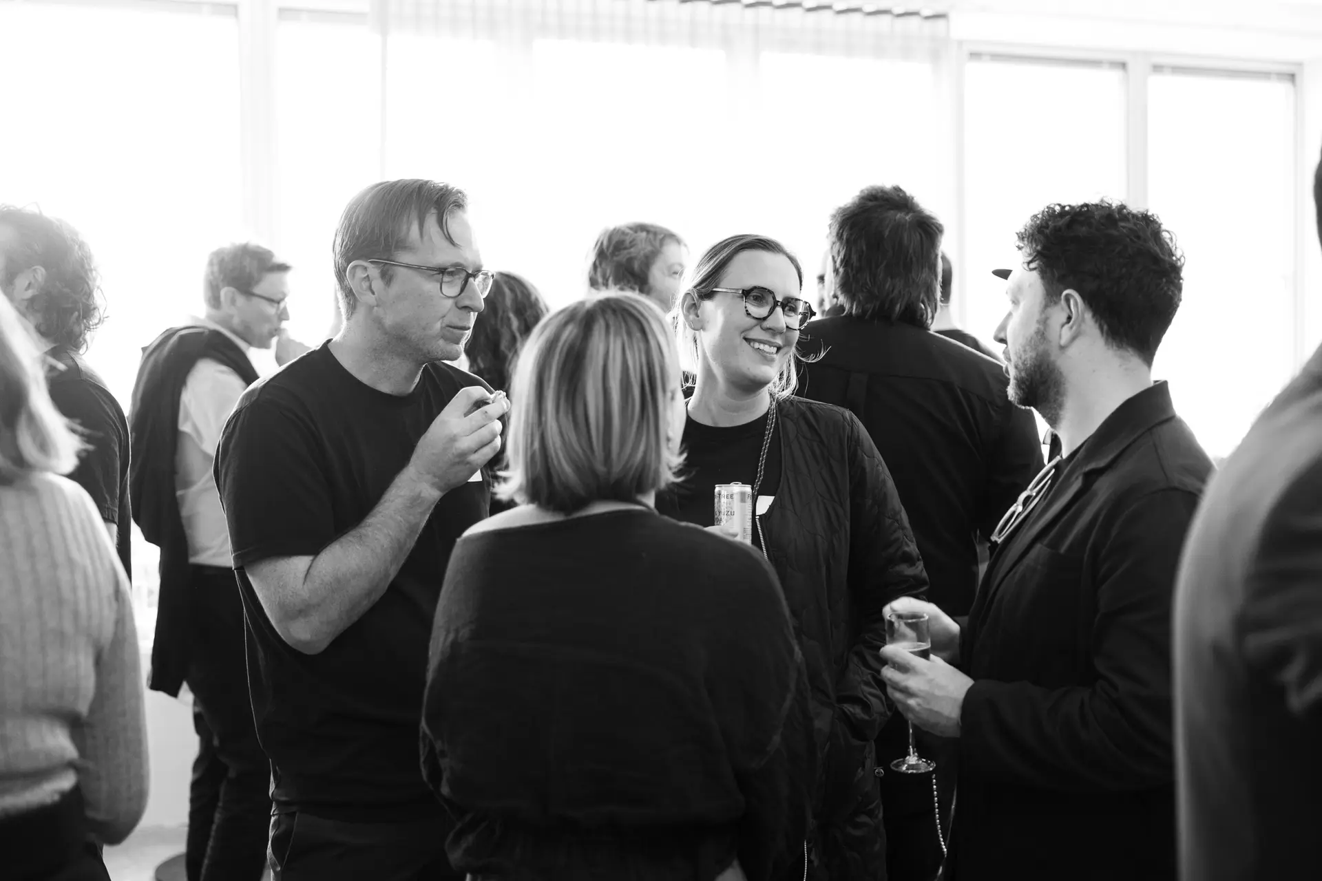 Black and white photo of a group of people in chatting and holding drinks at a social event.
