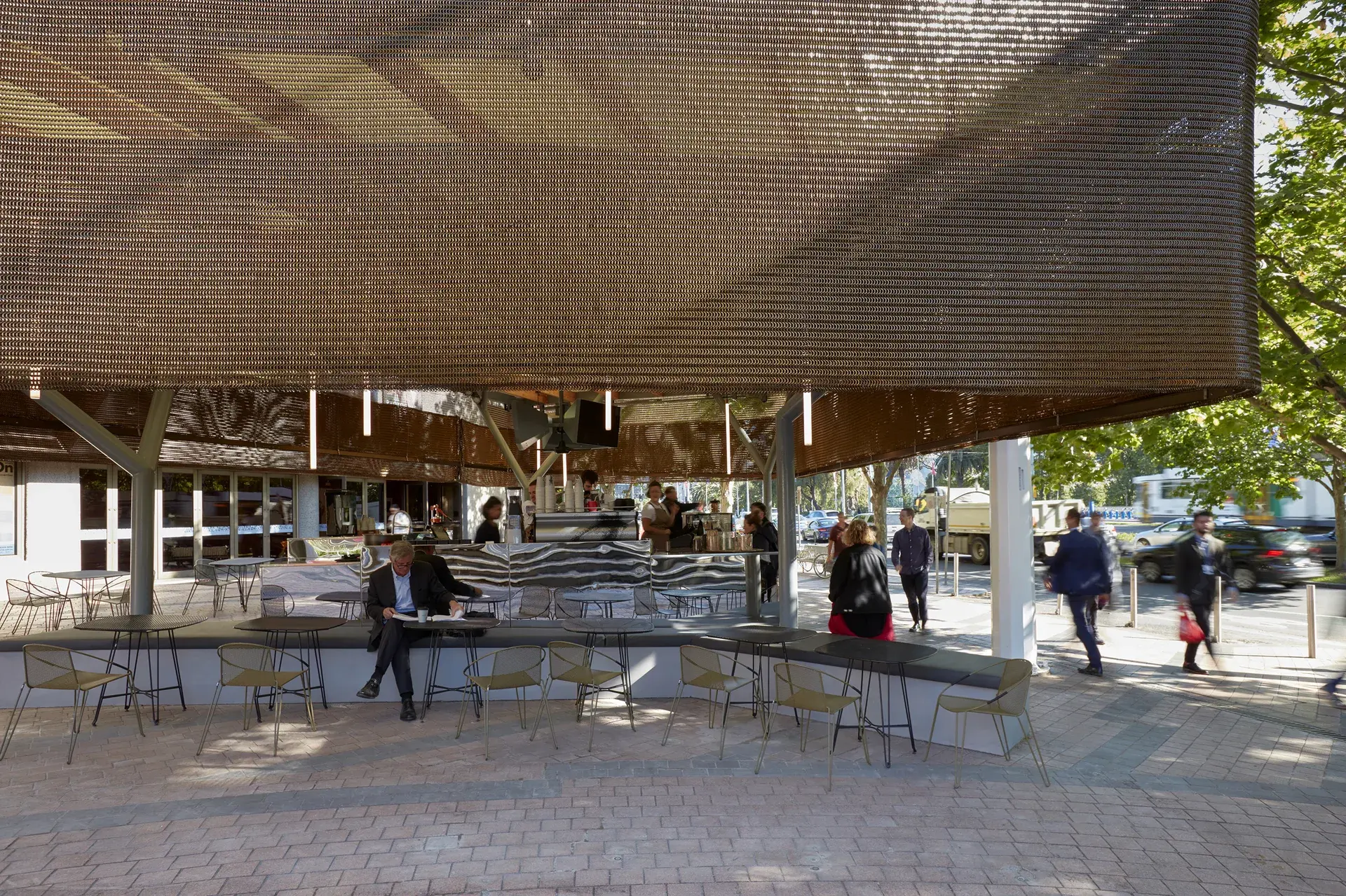 The Protagonist cafe in Melbourne, featuring a dramatic bronze chainmail curtain canopy that provides shade and a unique sculptural identity to the outdoor dining area.