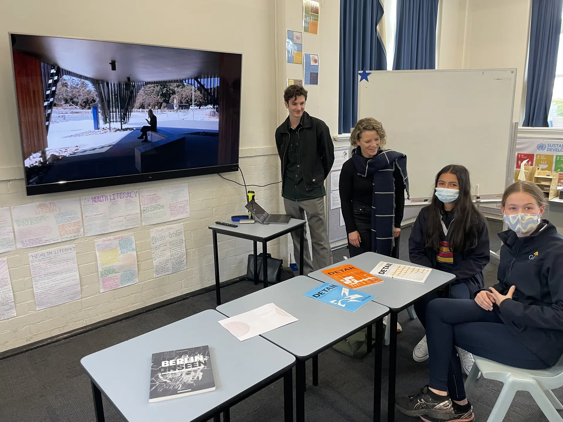 Ned Daniels and Ronja Scherer presenting to students in a classroom at Guilford Young College, with Cradle Mountain Visitors Centre displayed on a screen as students sit at desks reviewing materials.