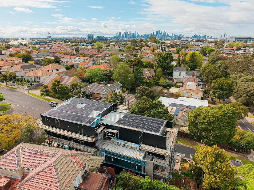 An aerial view of the Ascot Vale residence under construction with solar panels installed on its roof, situated in a suburban neighbourhood with the city skyline of Melbourne on the horizon.