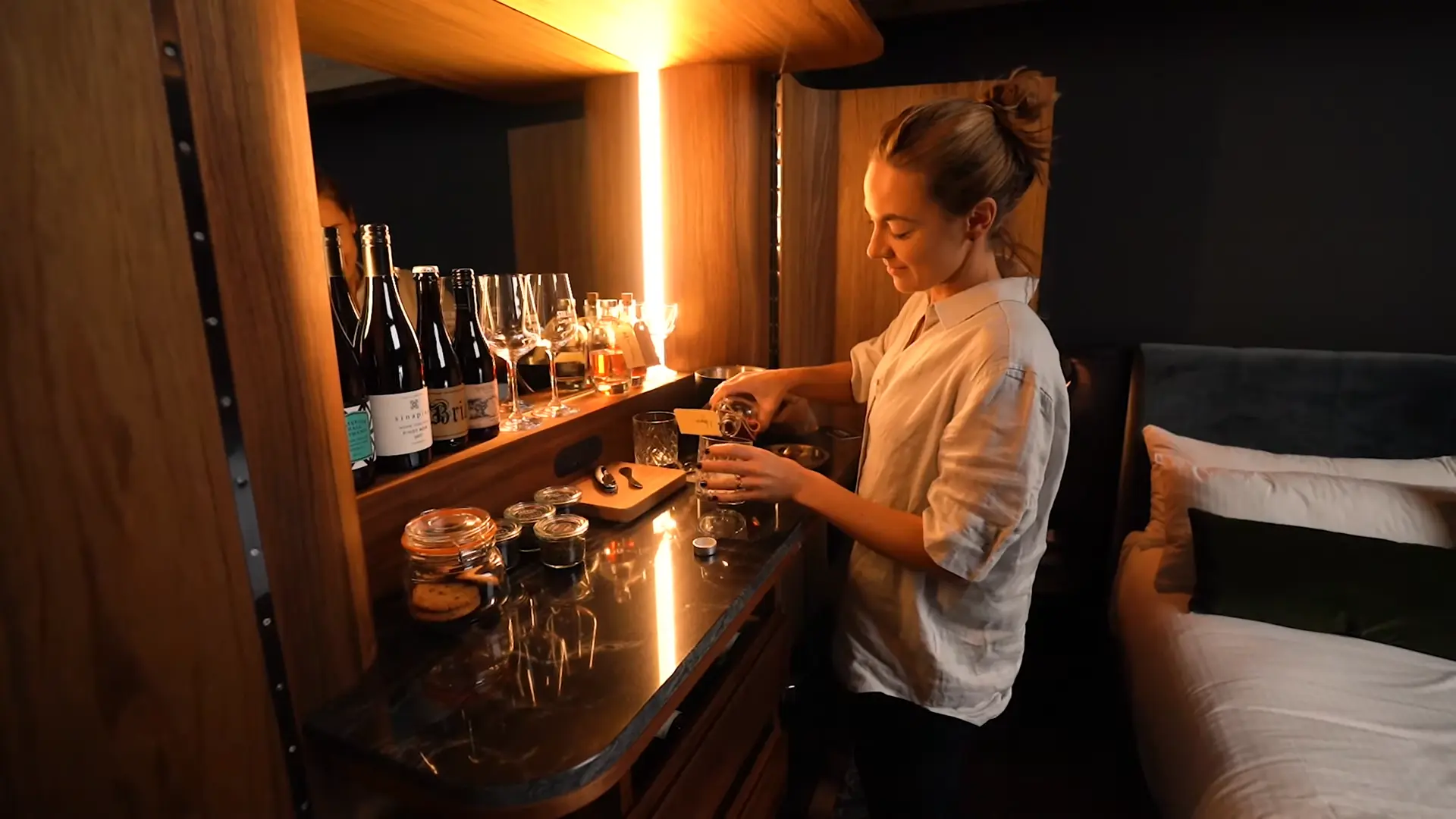 Lucy Glade-Wright prepares a drink at the custom cabinet minibar inside a Stillwater Seven room, with warm lighting and Tasmanian wood finishes.