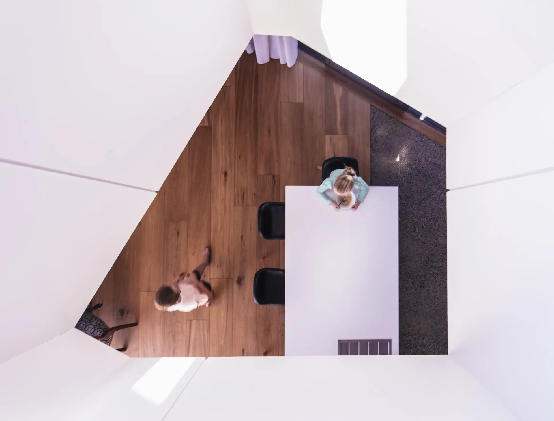 A top-down view of the dining space showing the junction between timber flooring and polished concrete, expressing the transition between habitable and service zones.