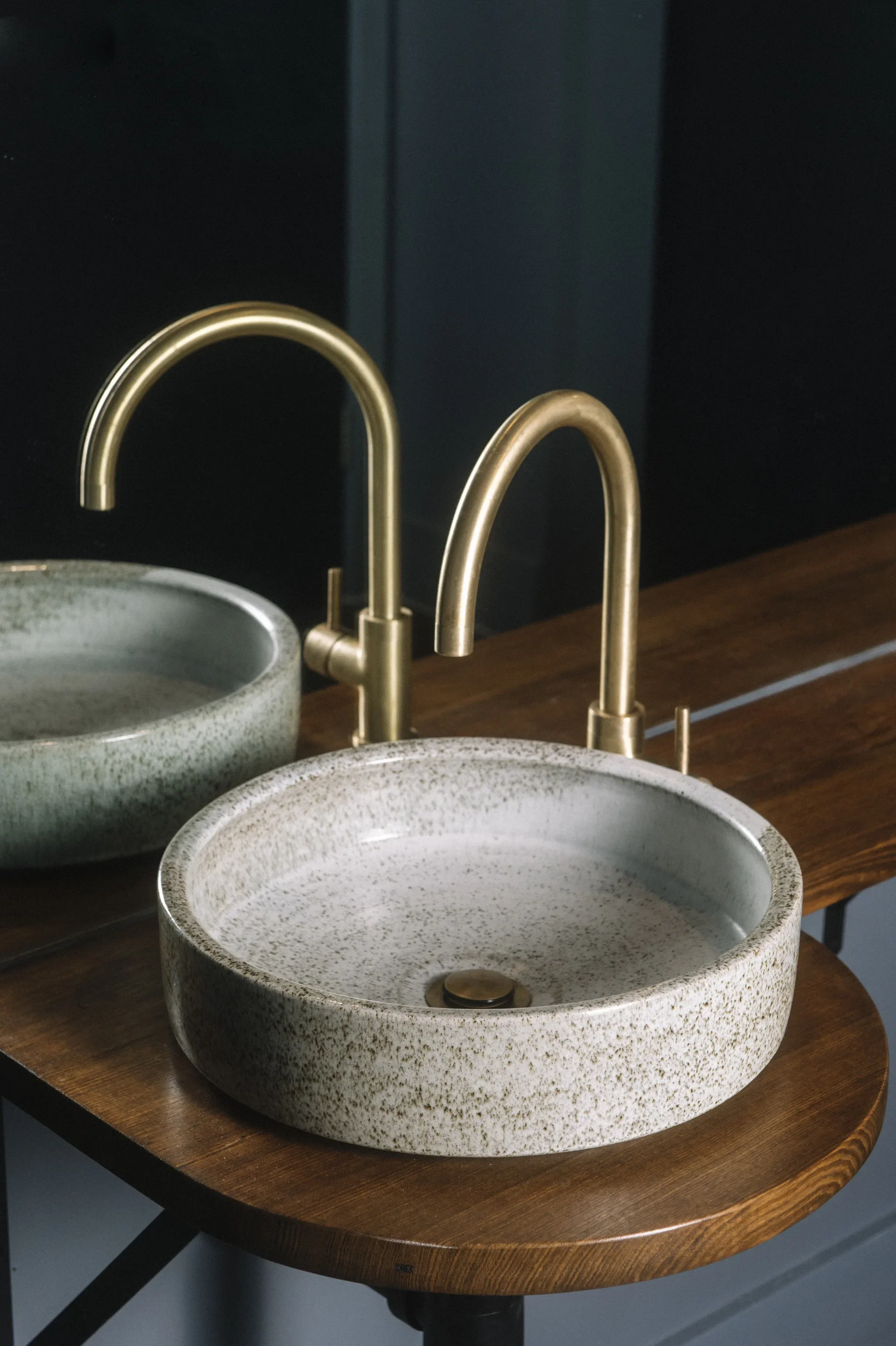 A speckled stone basin with a brass faucet sits on a timber vanity, set against a large mirror to highlight the interplay of natural textures and metallic accents.