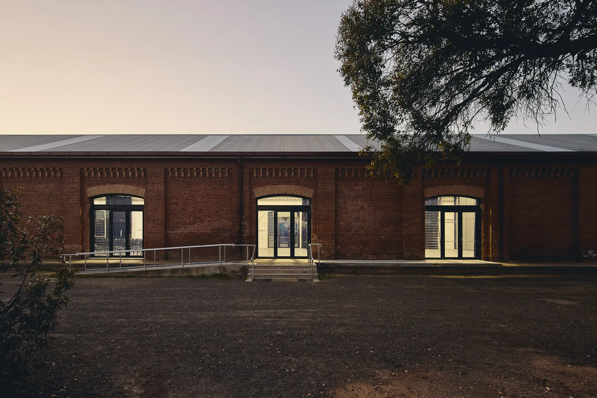 As dusk settles, a warm glow spills across the existing brick exterior and new glazed apertures, suggesting a renewed sense of place for the heritage building.