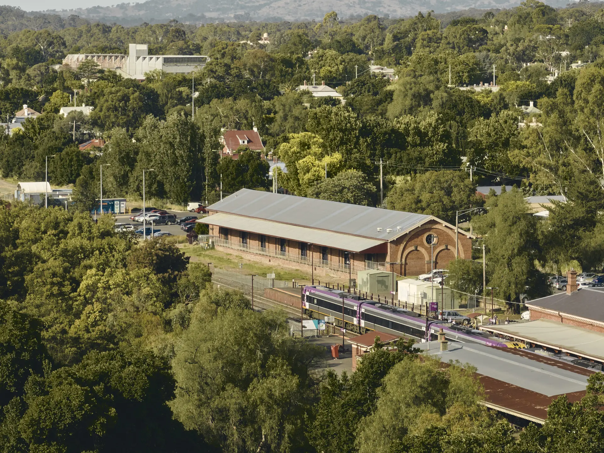 The Goods Shed, nestled within lush green surrounds and next to the train station, expressing a connection with its bustling rail history, community, and evolving public life.