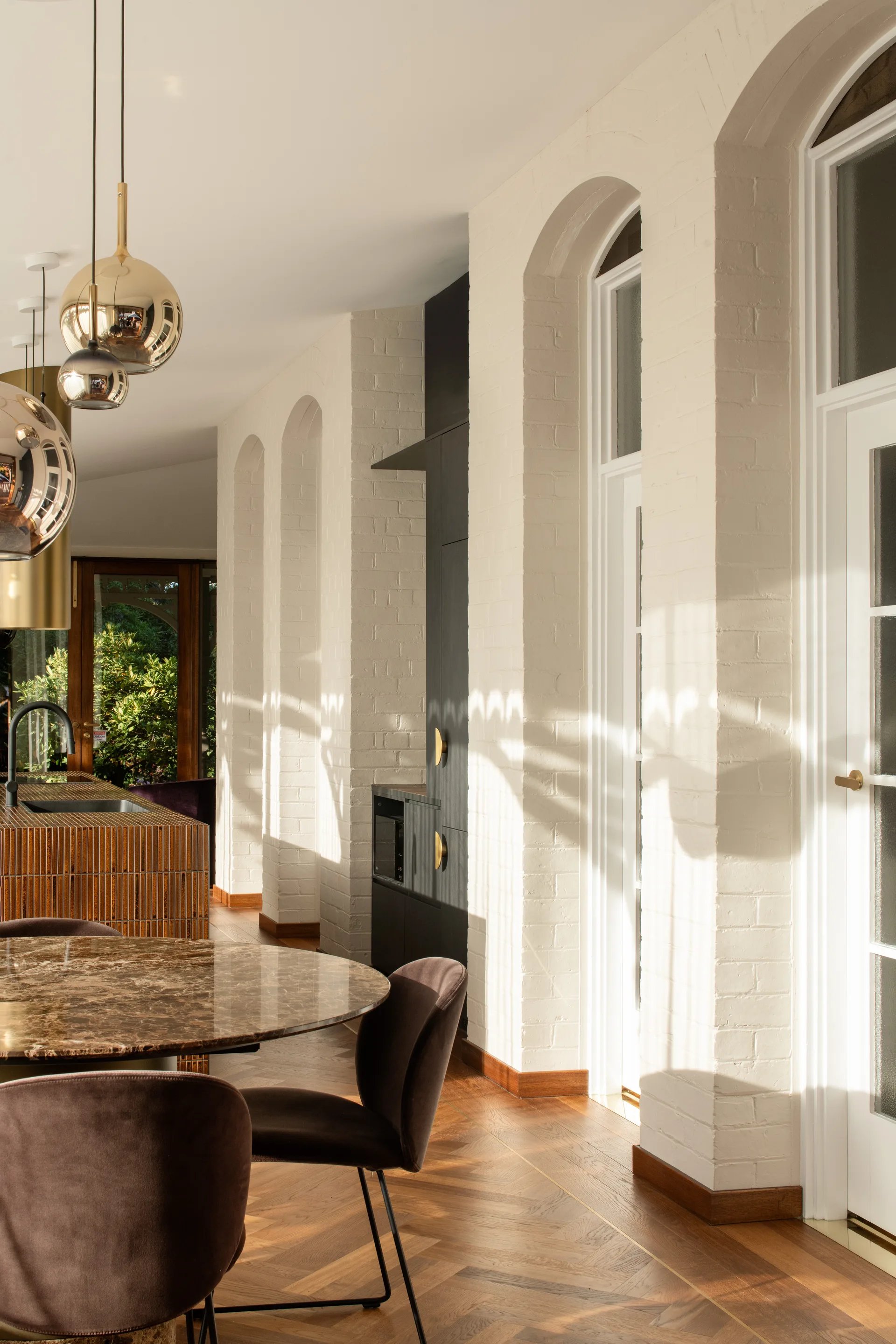 A detail shot, looking past the brown marbled circular table and suede brown seating arrangement, highlighting white painted brick walls of the existing external wall, lined with white doors and windows and feature dark panelled joinery.