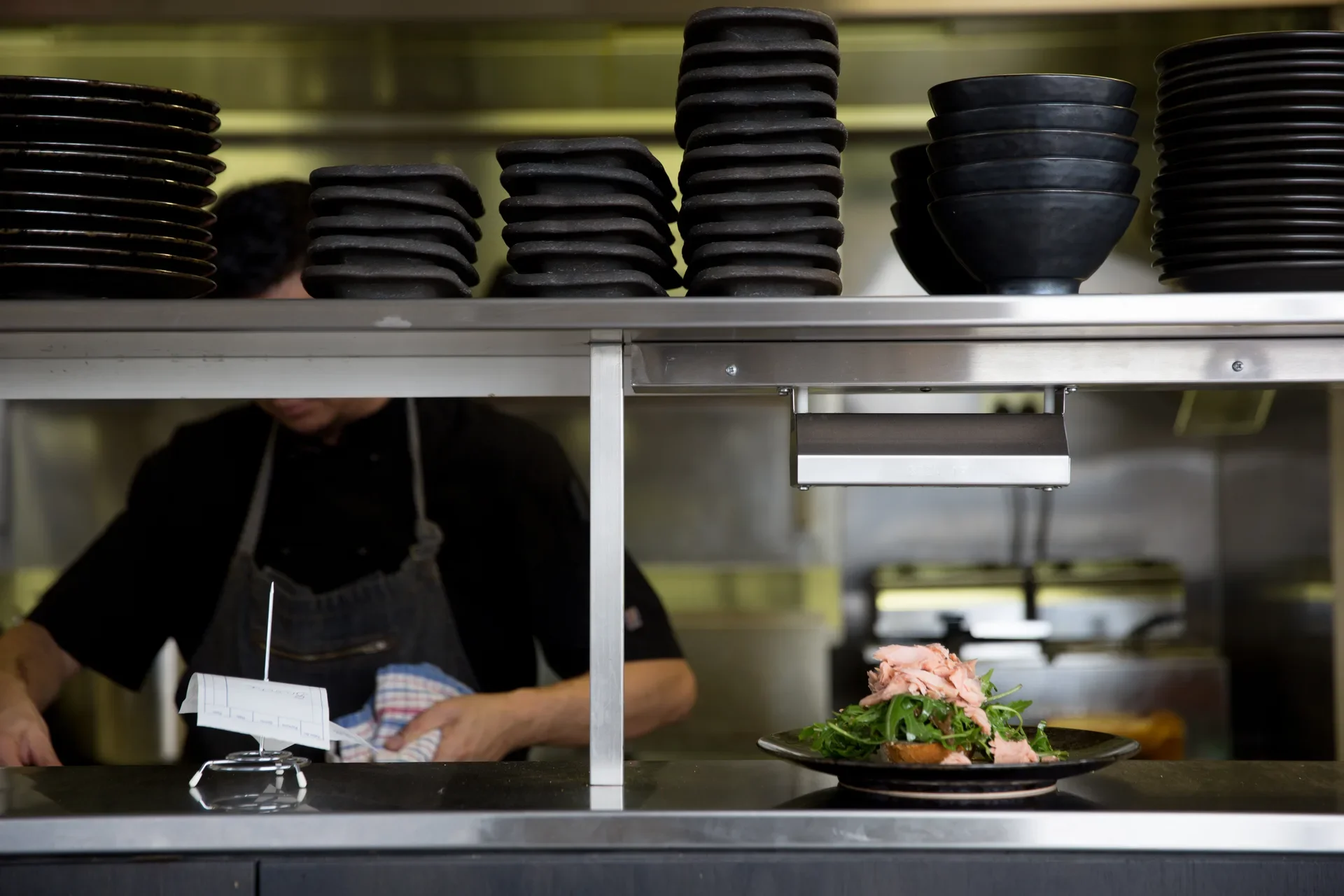A chef working behind stack of plates in the the commercial kitchen.