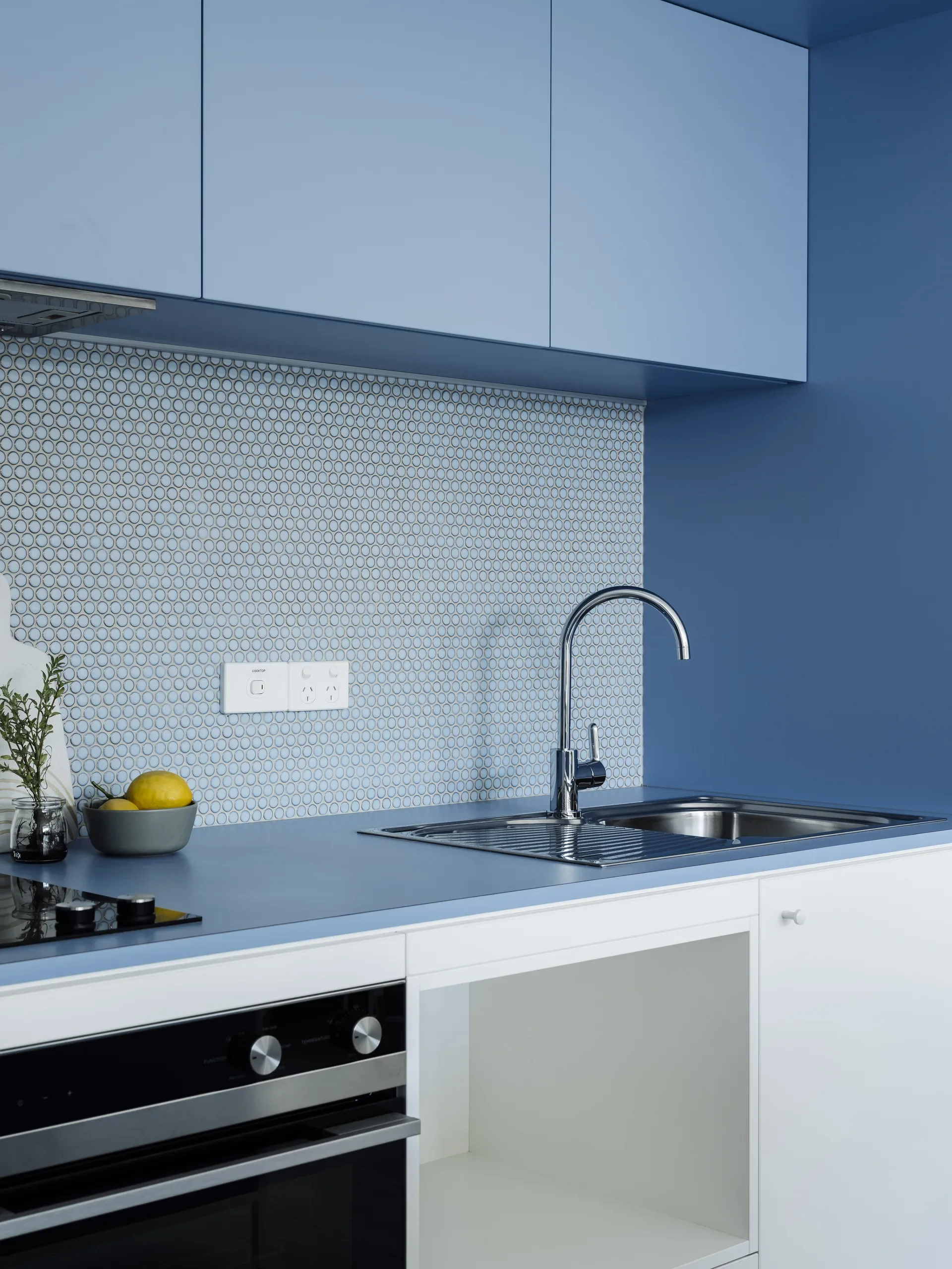 This modern kitchen features a blue countertop and upper cabinetry paired with a light blue penny tile backsplash and white lower cabinetry.