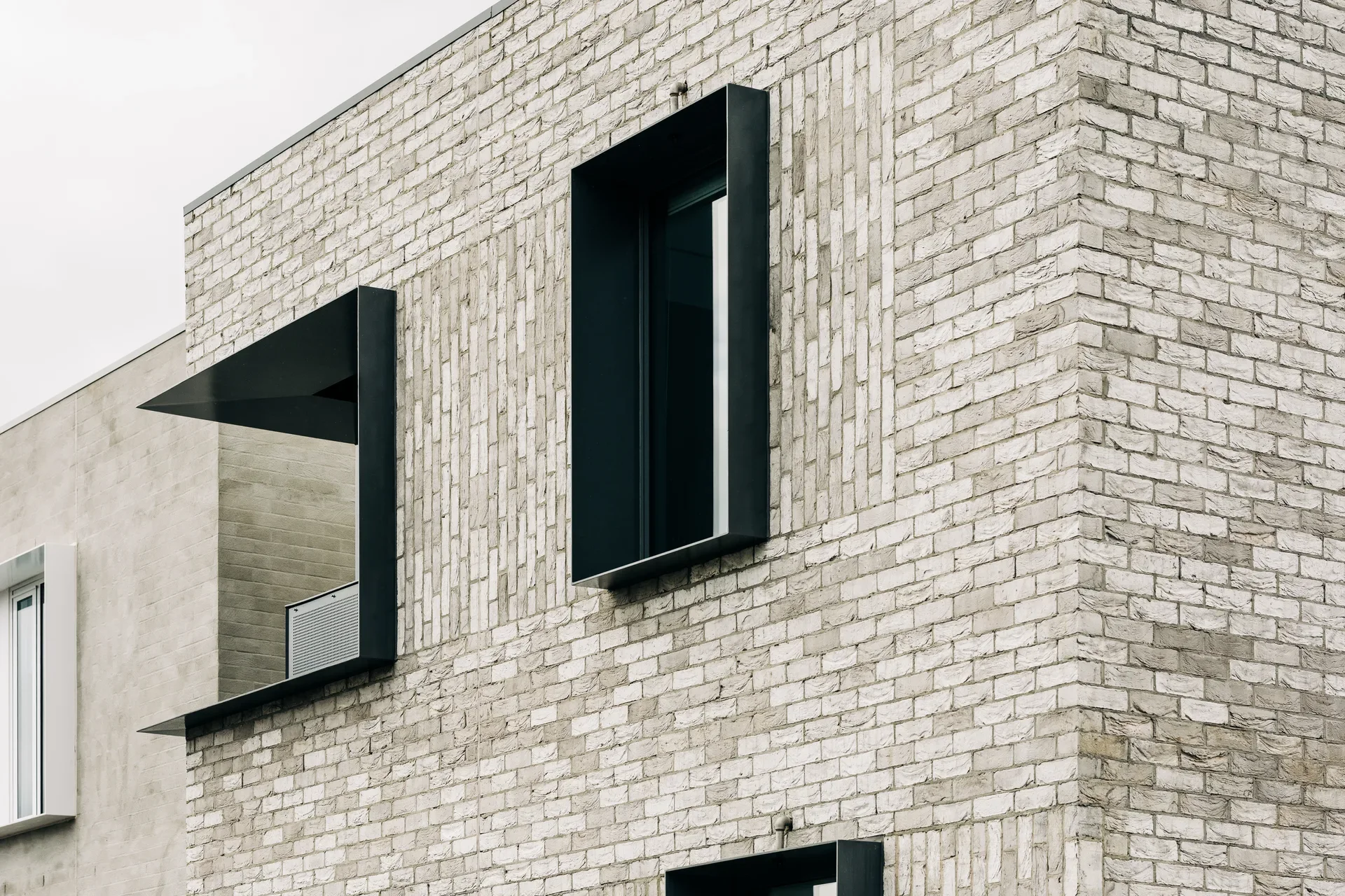 A light-coloured brick wall features deep-set windows framed in bold black metal, with vertical brickwork detailing between and to the sides of the openings.
