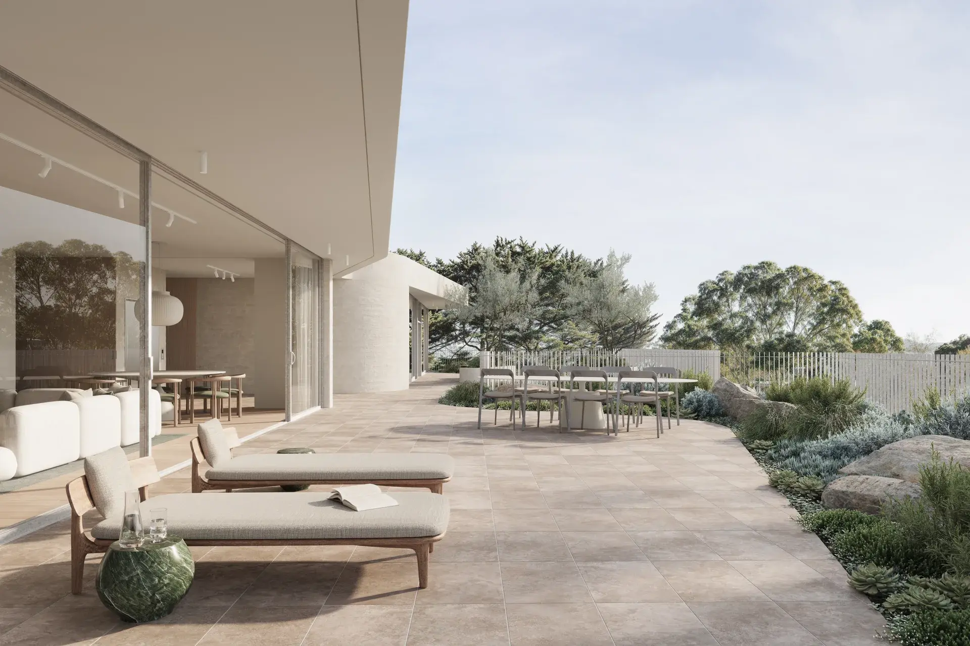 An architectural render of a penthouse terrace, viewed from a low, eye-level angle along a tiled outdoor space. Sliding glass doors open to an interior living area, while timber-framed loungers, a stone side table and an outdoor dining setting sit within landscaped edges of native planting, stone and low shrubs, framed by fine vertical balustrades overlooking tree canopy.