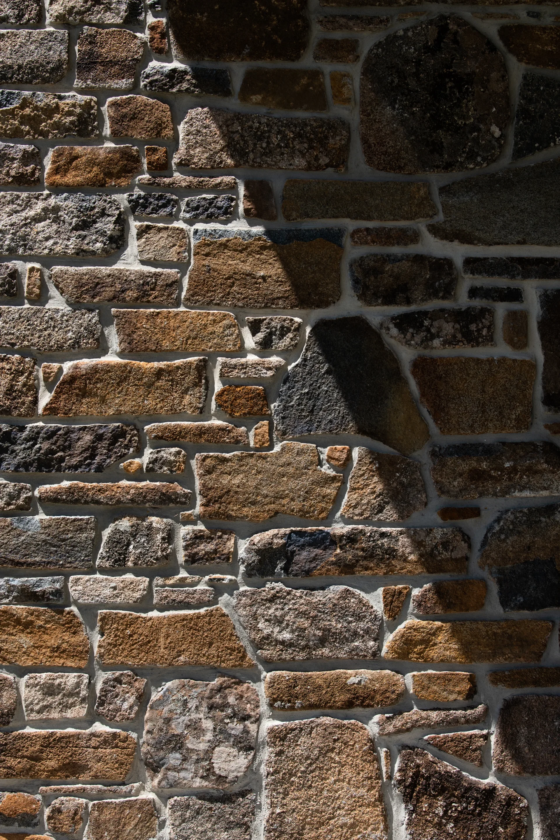 A close-up view shows a wall built from irregularly shaped fieldstones in various shades of brown, tan, and grey, held together by light-coloured mortar.