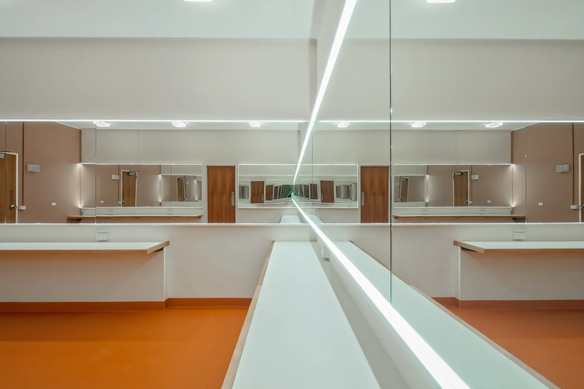 A bright dressing room features an orange floor, white counters, and large mirrors with integrated LED lighting that create an infinite reflection.