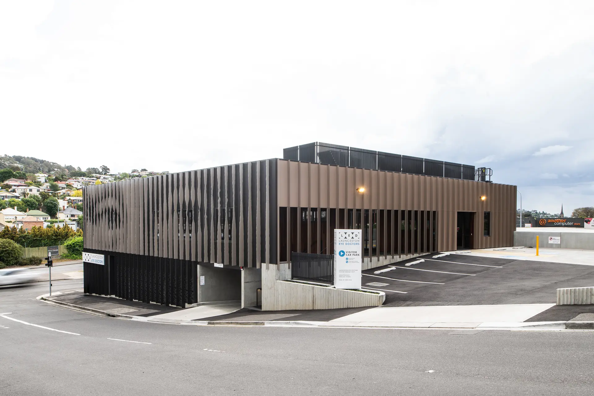 The exterior of Launceston Eye Doctors, showcasing a rhythmic vertical slat design, visitor parking, and a prominent white directional sign.