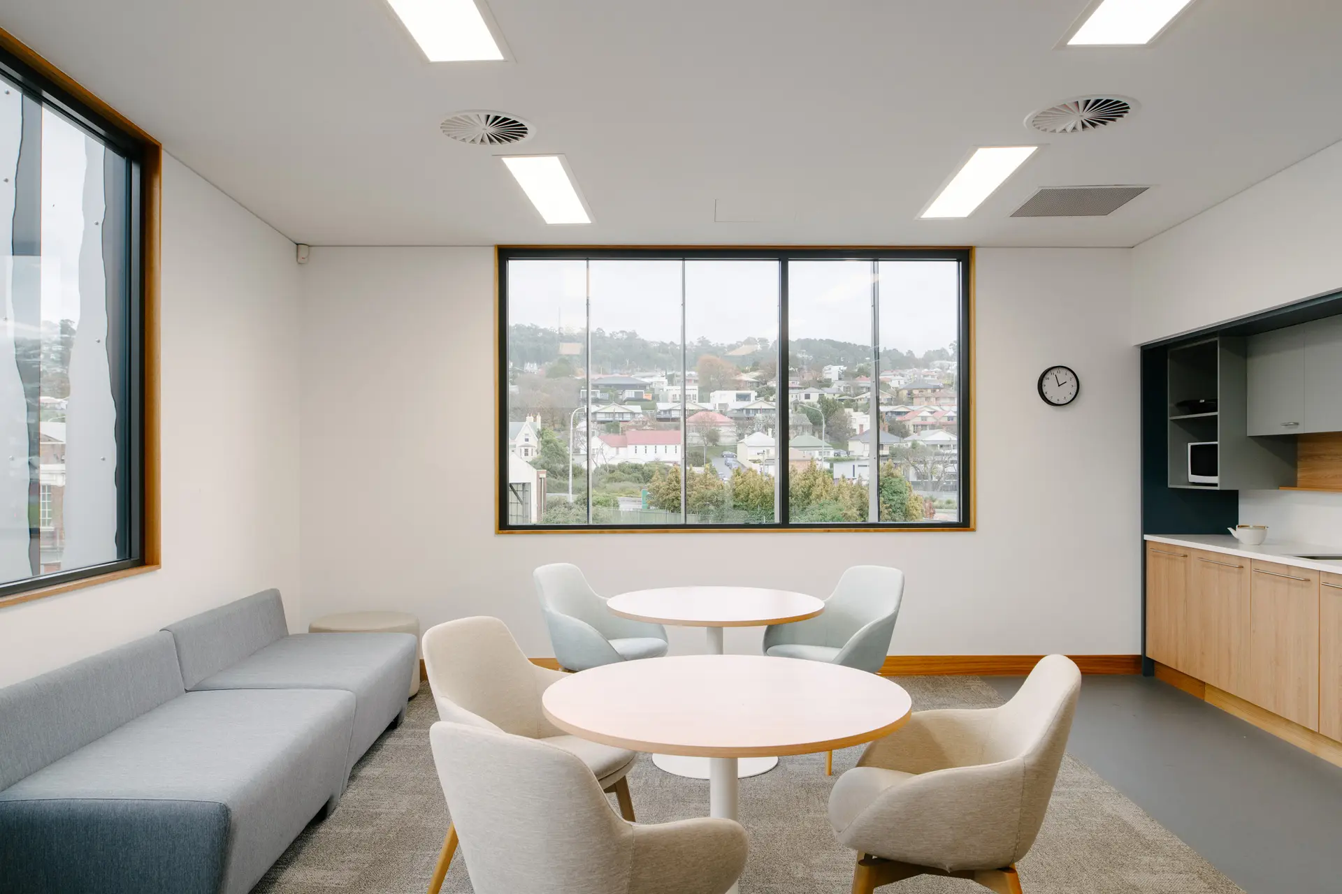 A spacious, sunlit room with contemporary furniture, warm wood accents, and a large digital screen displaying a scenic landscape photo.