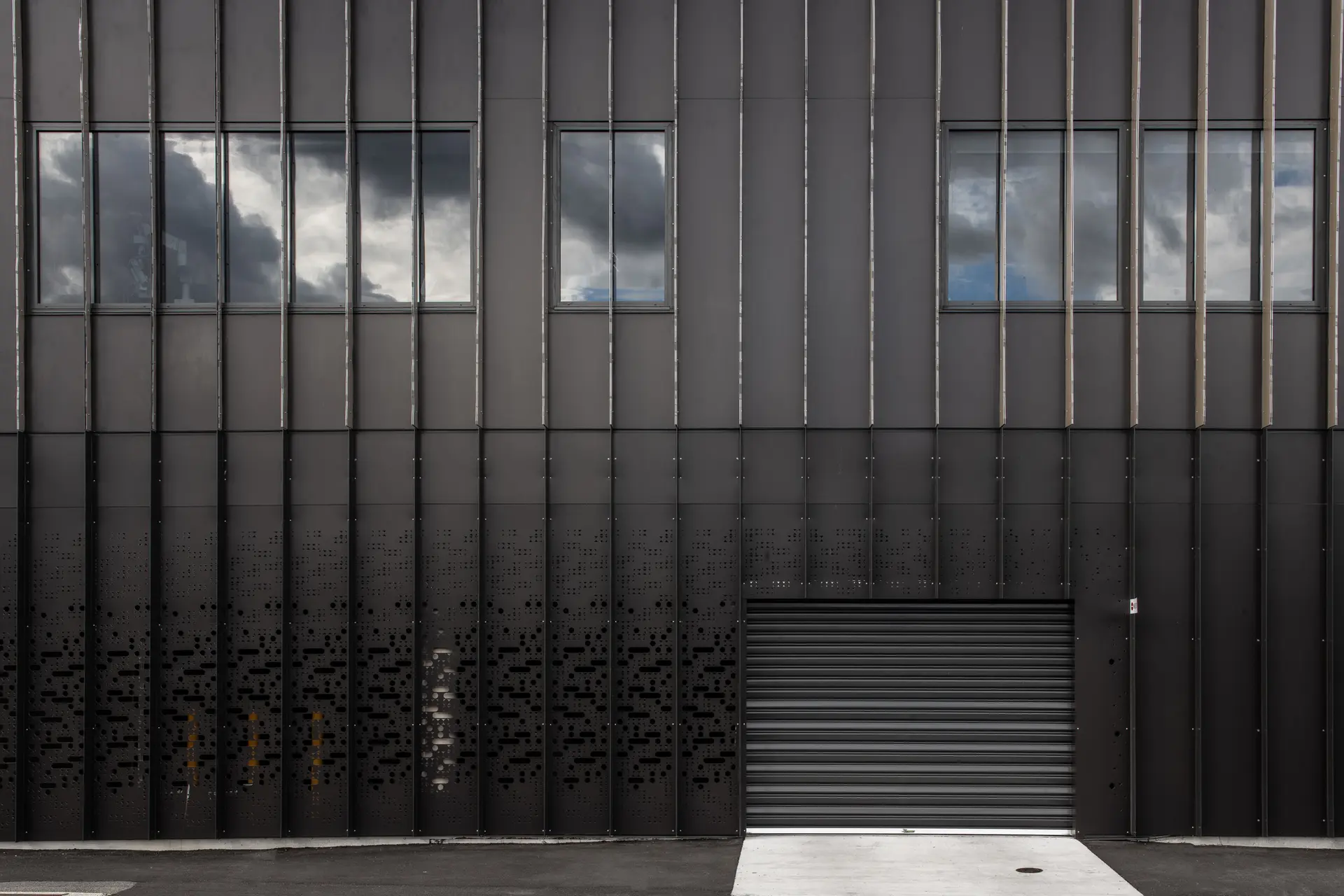 A dark industrial building exterior with vertical fins, perforated metal patterns.
