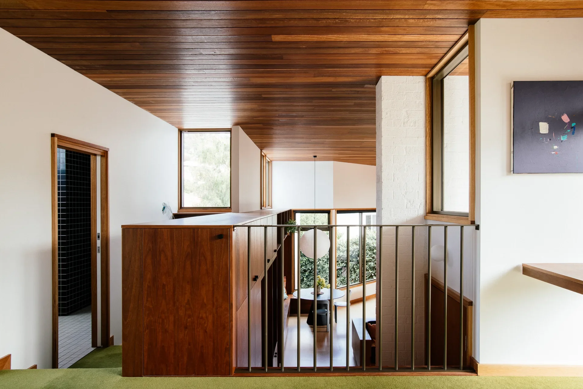 Upper-level view of a modern home featuring slatted timber ceilings, white brick pillars, and a metal-railed mezzanine.