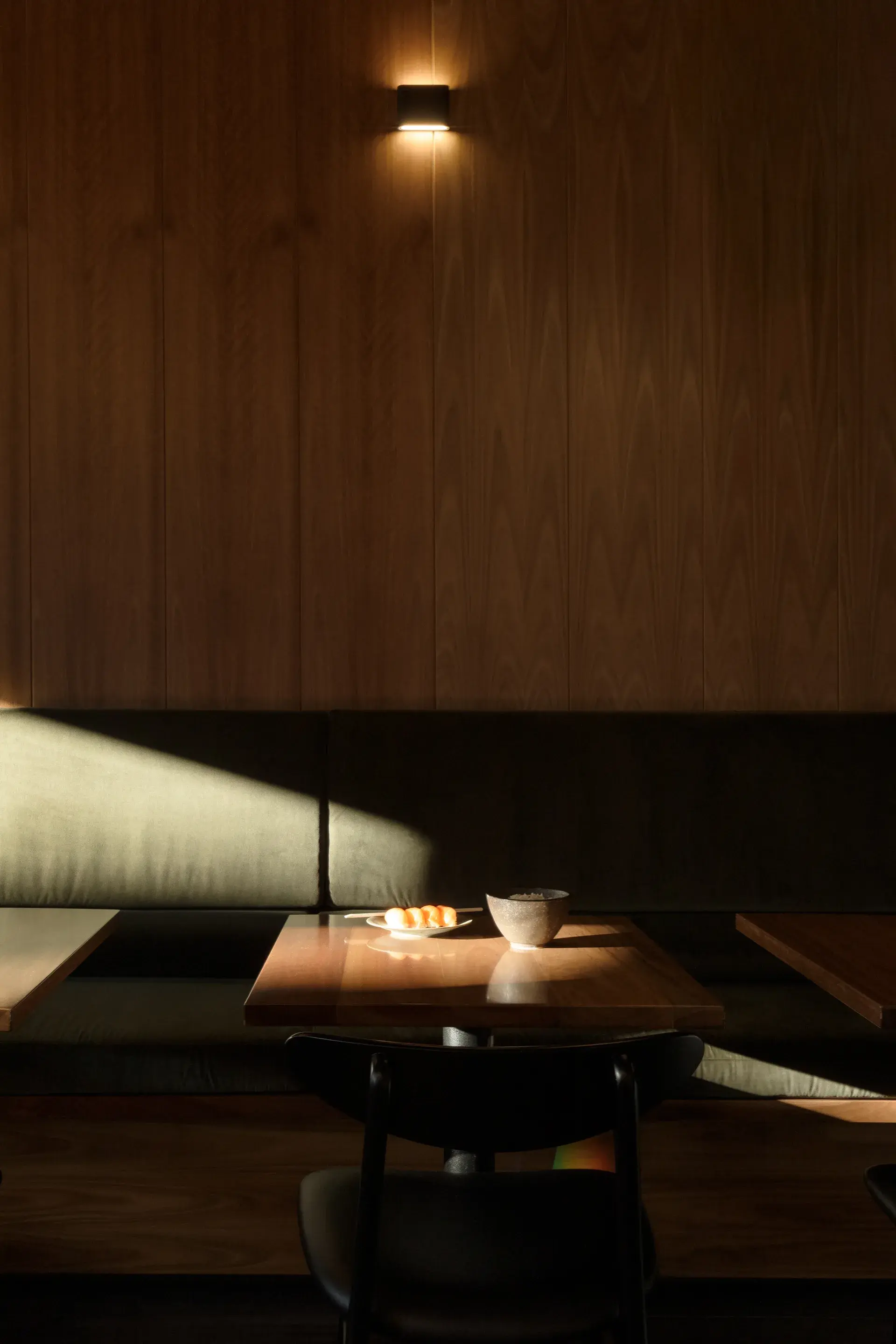 Natural light through heritage windows casts shadows across green velvet bench seating, spotted gum timber wall panels and custom dining tables.