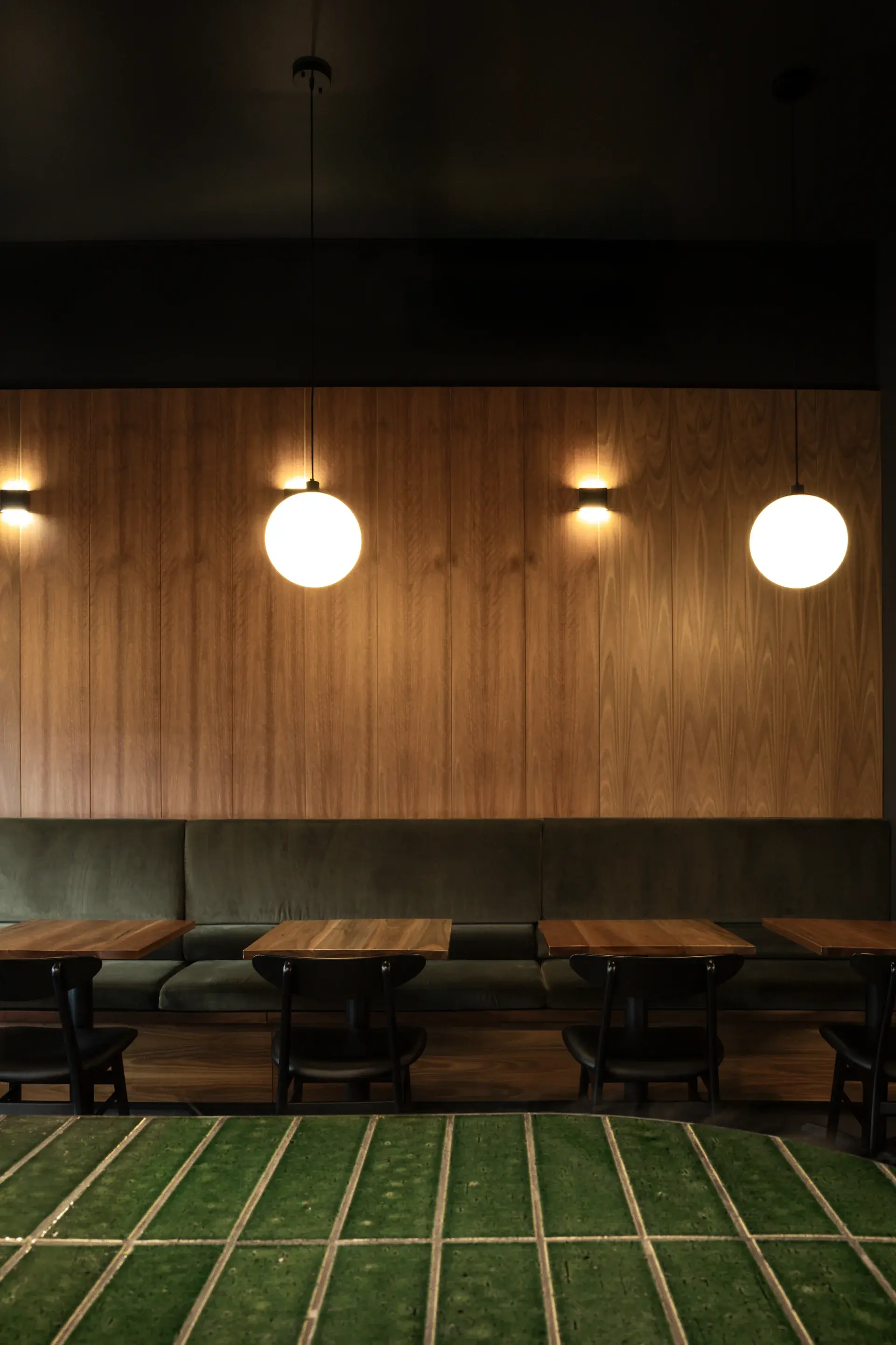 Glass orb pendants above dining tables offer a modern take on paper lanterns, with velvet seating, green tile and timber panelling in harmony.