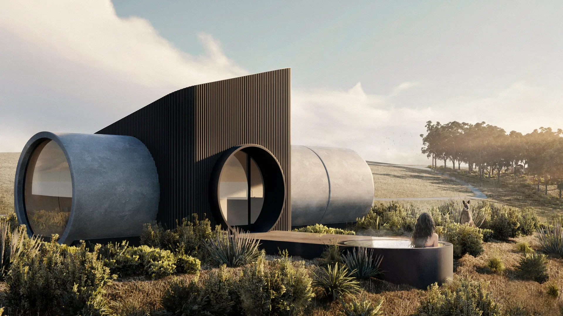 Minimalist timber cabin with an angled roof perched on a grassy hill. Large windows reveal a warm interior, with a figure on the deck overlooking the expansive landscape.