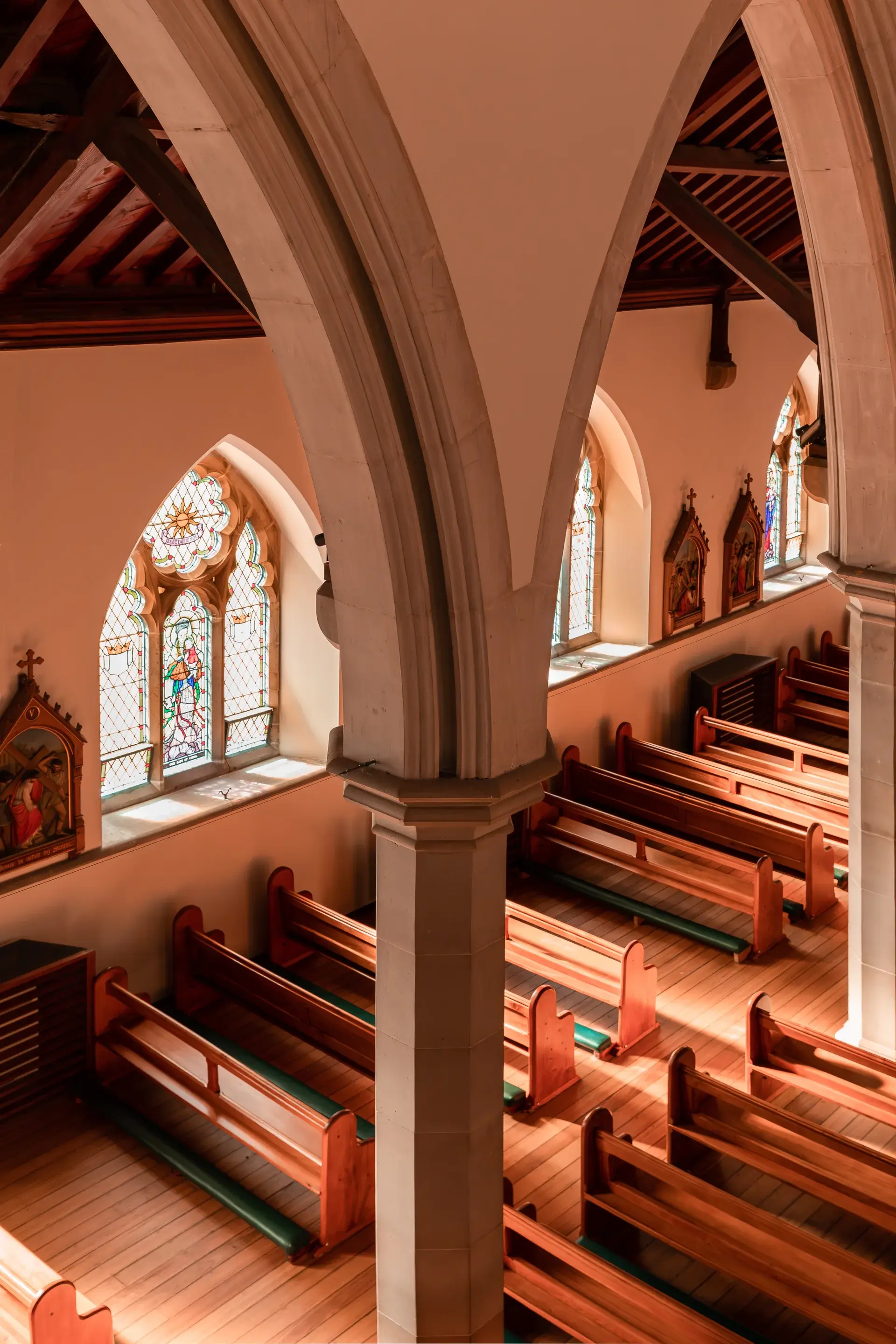 A high-angle view of the interior featuring stone pillars and pointed arches, overlooking rows of wooden pews and arched stained-glass windows.