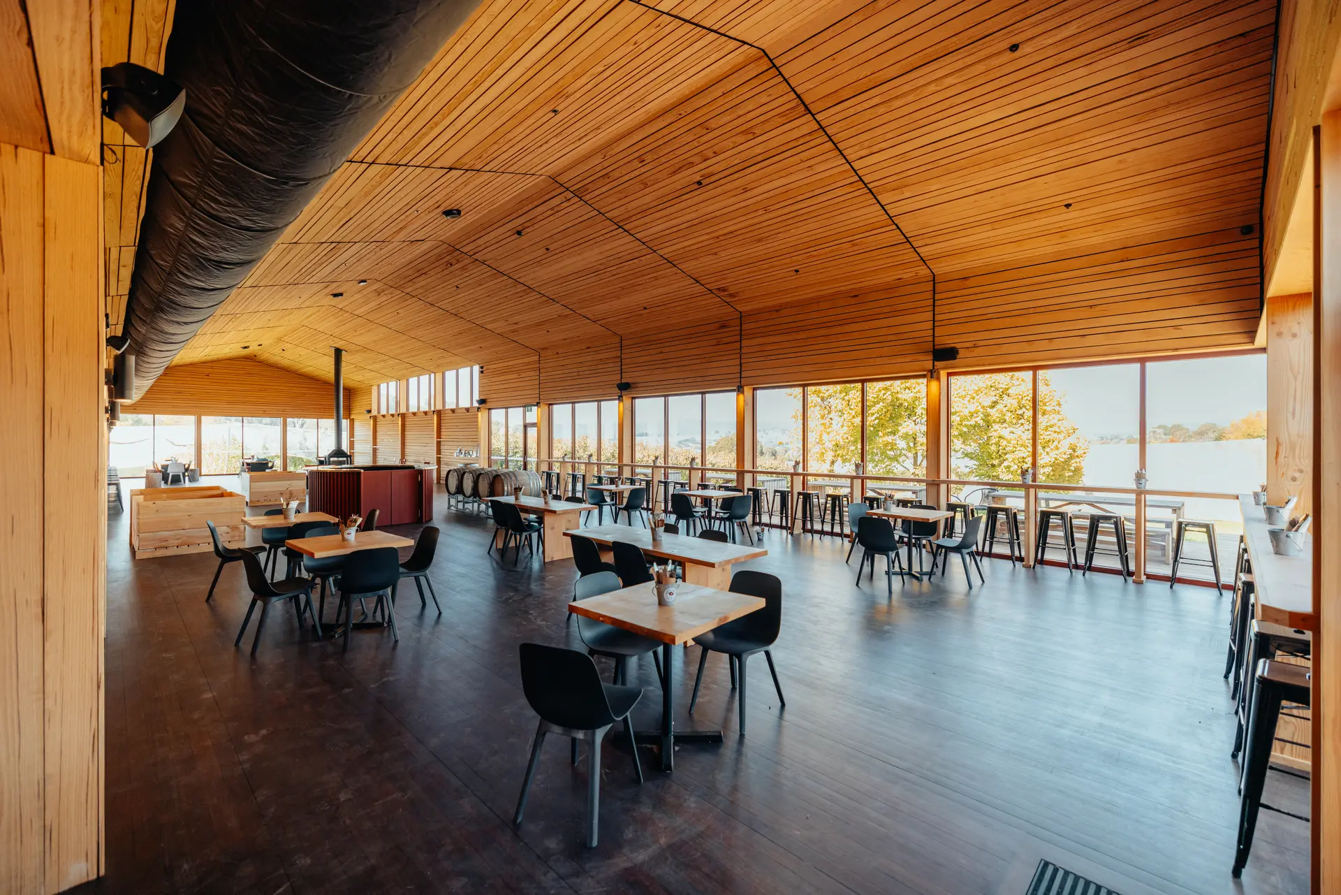 A long, red corrugated metal building with large windows and a wooden deck featuring outdoor picnic tables at sunset.