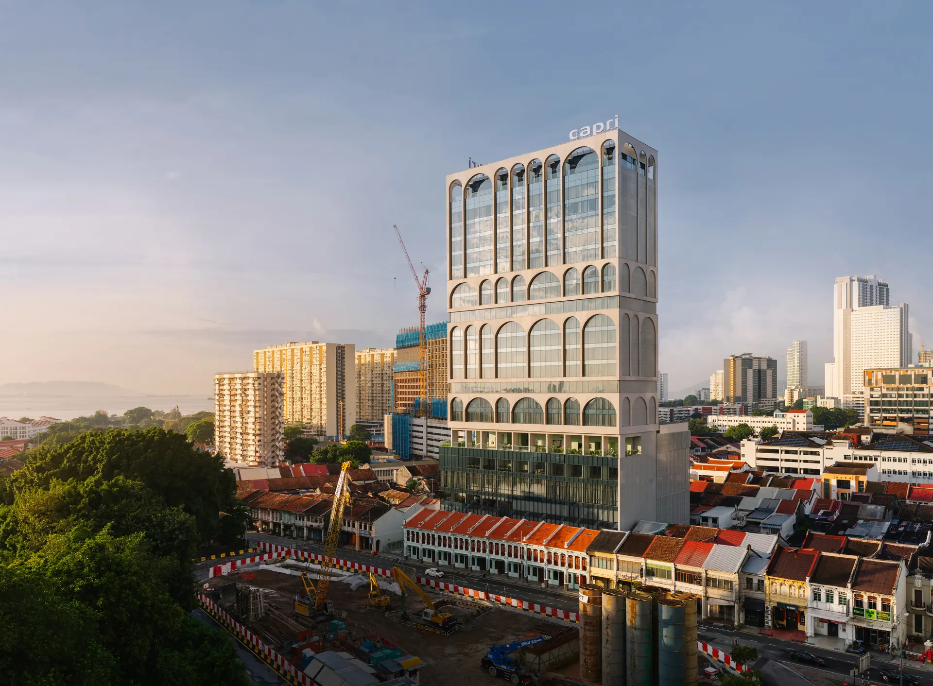 A tall tower of a hotel building, standing in the context of surrounding shopfronts and houses on a street in George Town in Penang.