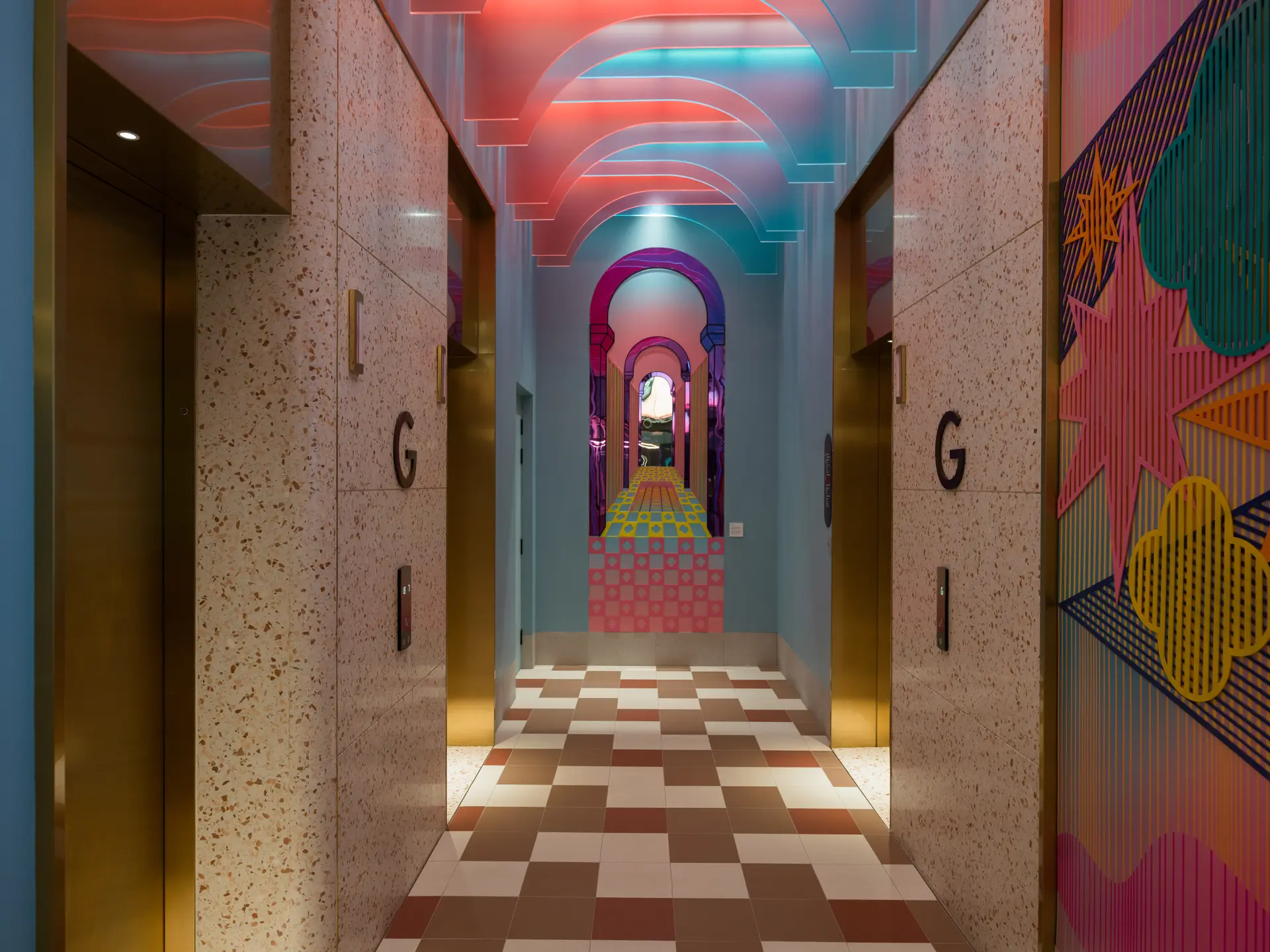 A lift lobby area, with pink and blue lighting, brown and cream tiled floors.