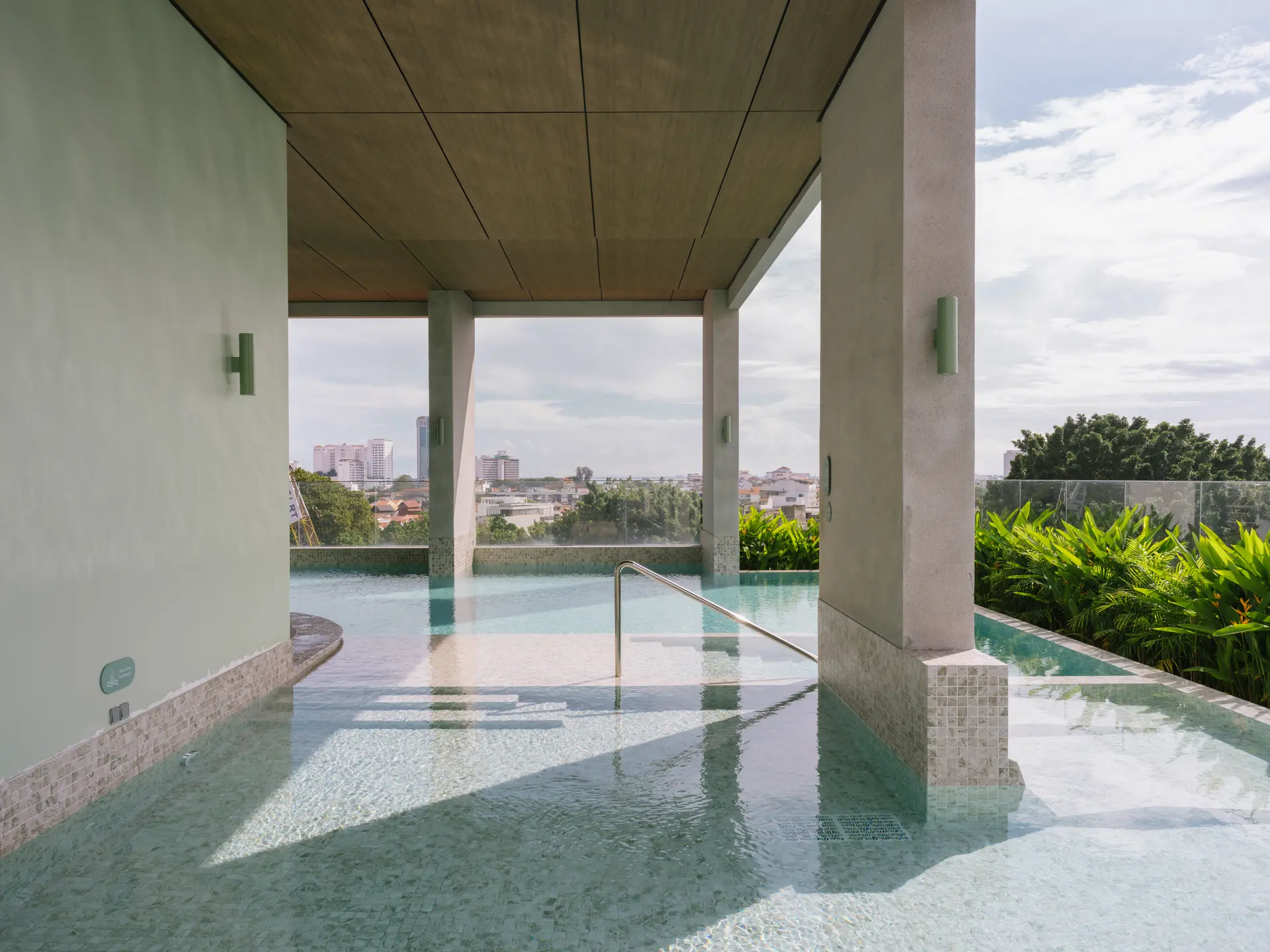 Rooftop pool at Capri Penang framed by timber-clad columns, overlooking George Town's rooftops and skyline.