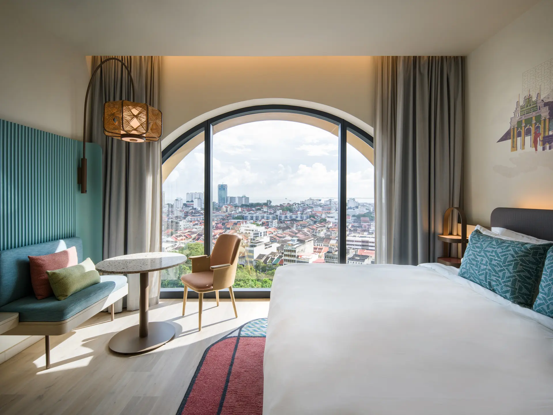 A Capri Penang guest room with a teal banquette and terrazzo side table beside an arched window overlooking George Town.