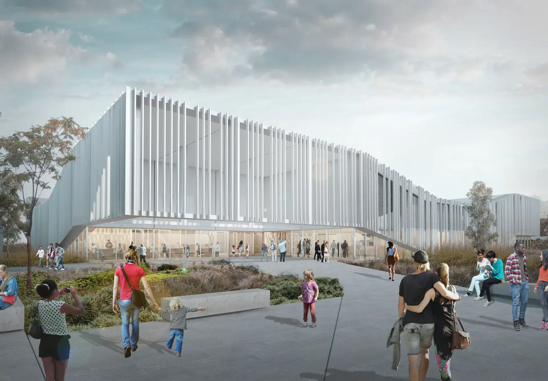 People walk toward a large, modern building with a distinct white slatted facade and glass-walled entrance. In the foreground, visitors gather on a paved plaza featuring concrete benches and low-lying vegetation.