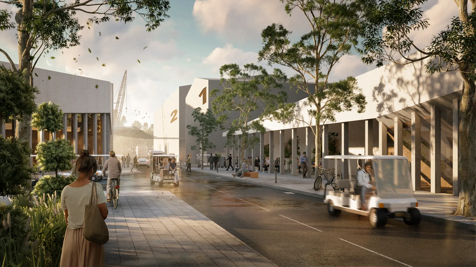 An architectural render from a street-level perspective along a studio lot boulevard, framed by colonnaded buildings with repetitive concrete columns and deep overhangs. Large, simple volumes marked with stage numbers “1” and “2” sit behind, while people move through the space on foot, bicycles and small utility carts. Native planting and street trees soften the edge, and warm, low-angle light casts long shadows, giving the precinct an active yet controlled studio environment.