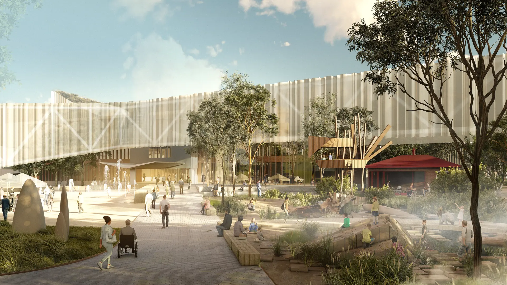 A visualisation of the master plan looking through the main public space, foregrounded by kids playing within the wet and dry play areas, climbing rock formations and a wooden treehouse enveloped with an established native garden. The image looks toward the elongated polycarbonate addition glowing atop the existing heritage building, now the entrance to the new library. A cafe and plaza with water fountains can also be seen to the sides of the illustration.