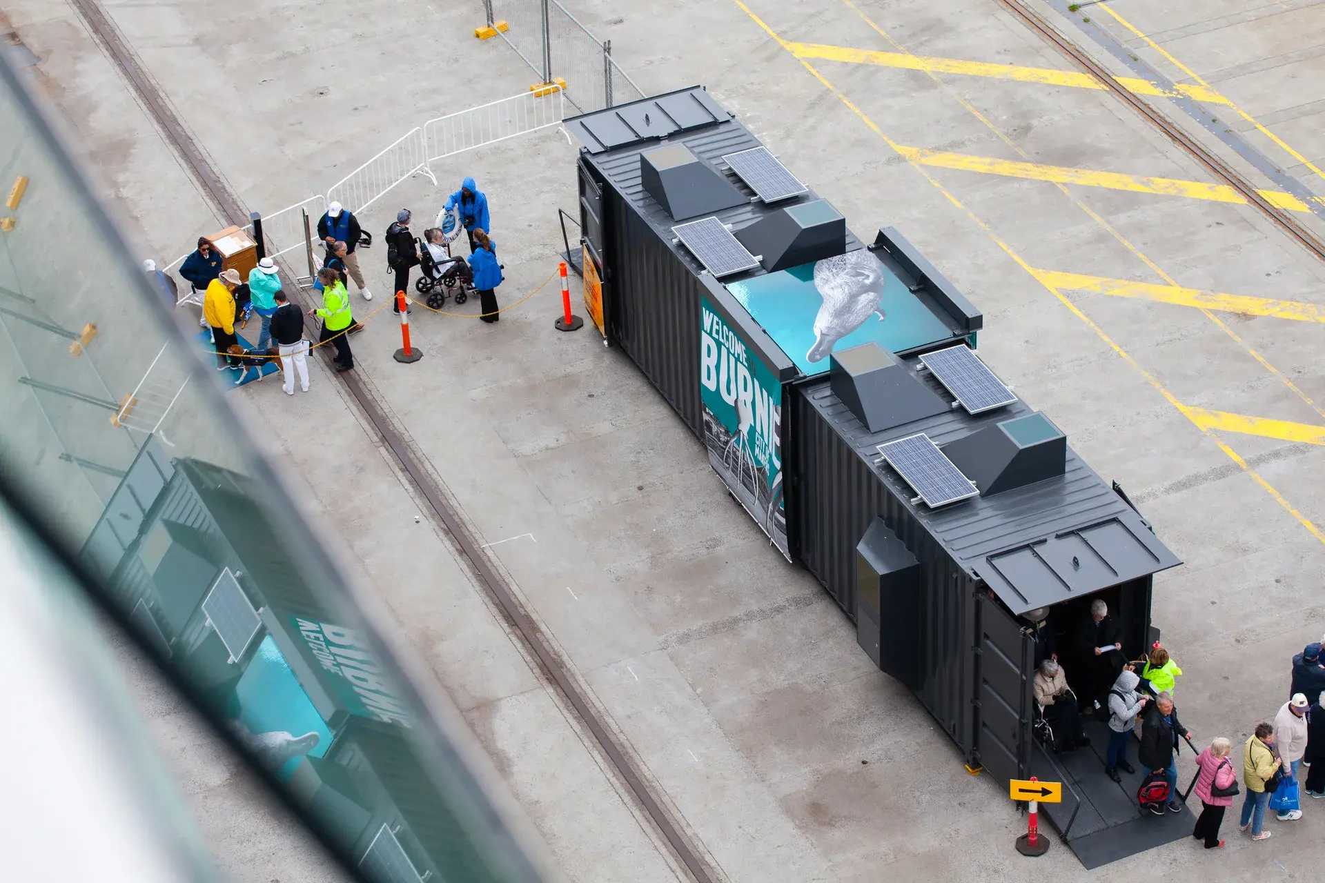 A group of tourists including someone in a wheelchair entering the second shelter. Futago's roof top graphic of a Platypus can be seen on this shelter, alongside an enormous blue and white Welcome to Burnie graphic on the side.