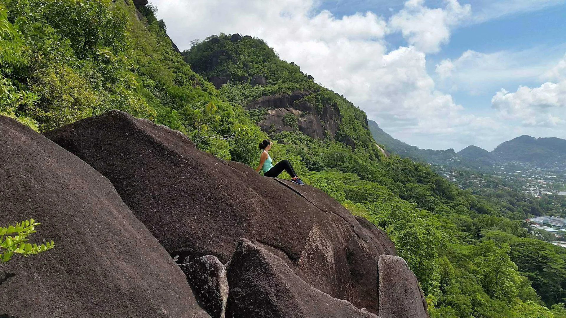 Sitting atop big beautiful granite boulders, with mountains and lush green vegetation in the backdrop, looking towards the small town of Victoria in the Seychelles.
