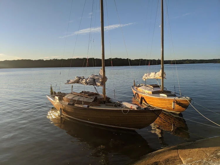 Two wooden sailboats resting on calm water at golden hour, their masts reflected in the still surface.