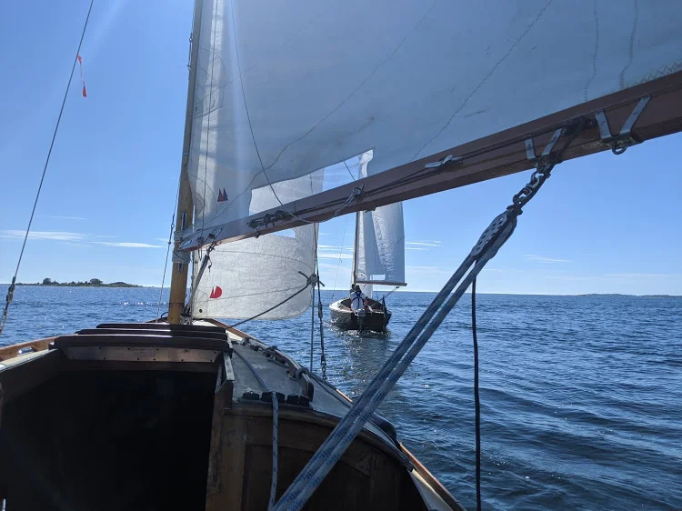 A view from aboard a sailboat looking out across open water, with sails raised and another boat ahead.