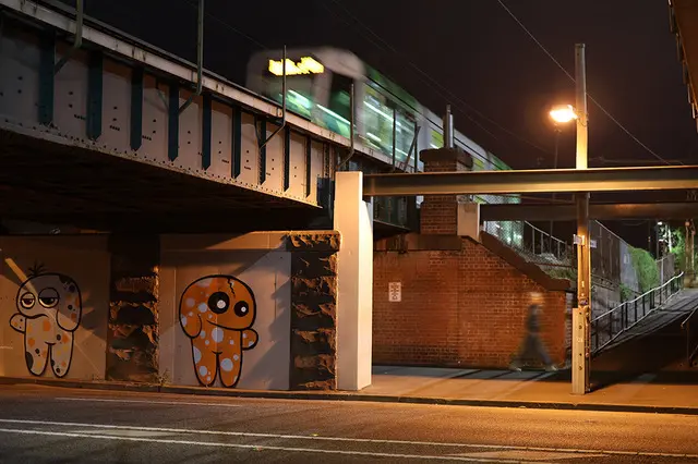 Urban night scene under an overpass, capturing a pedestrian in motion with a tram moving overhead