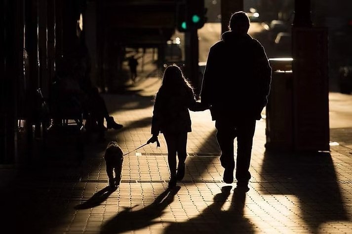 Pete and his daughter walking their small dog along a street in the middle of Hobart Tasmania, silhouetted by the low winter sunlight.